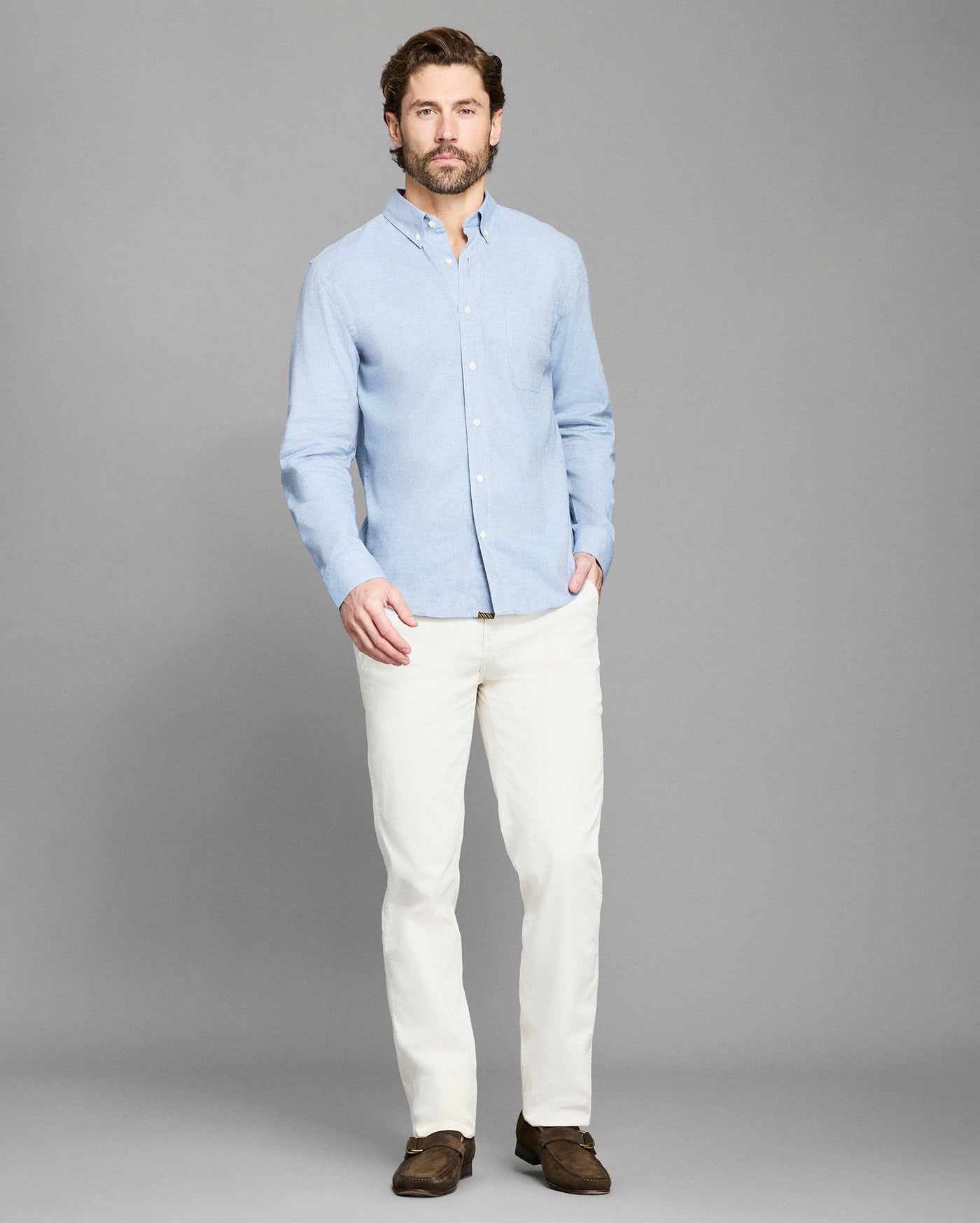 Man wearing a light blue shirt and white pants on a gray background