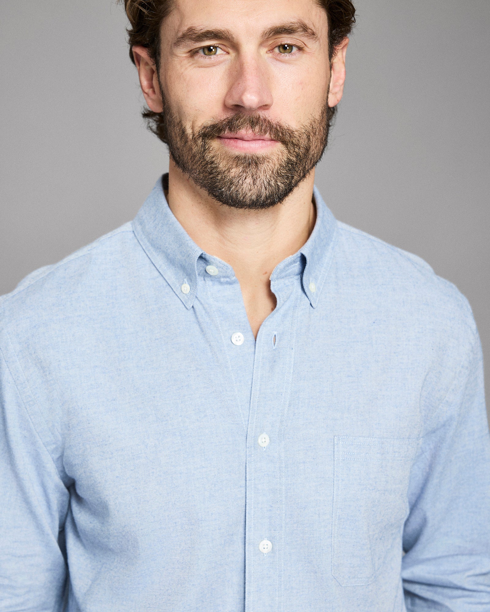 Man wearing a light blue button-up shirt against a gray background