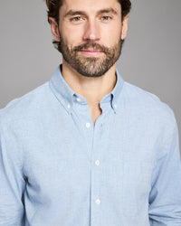 Man wearing a light blue button-up shirt against a gray background