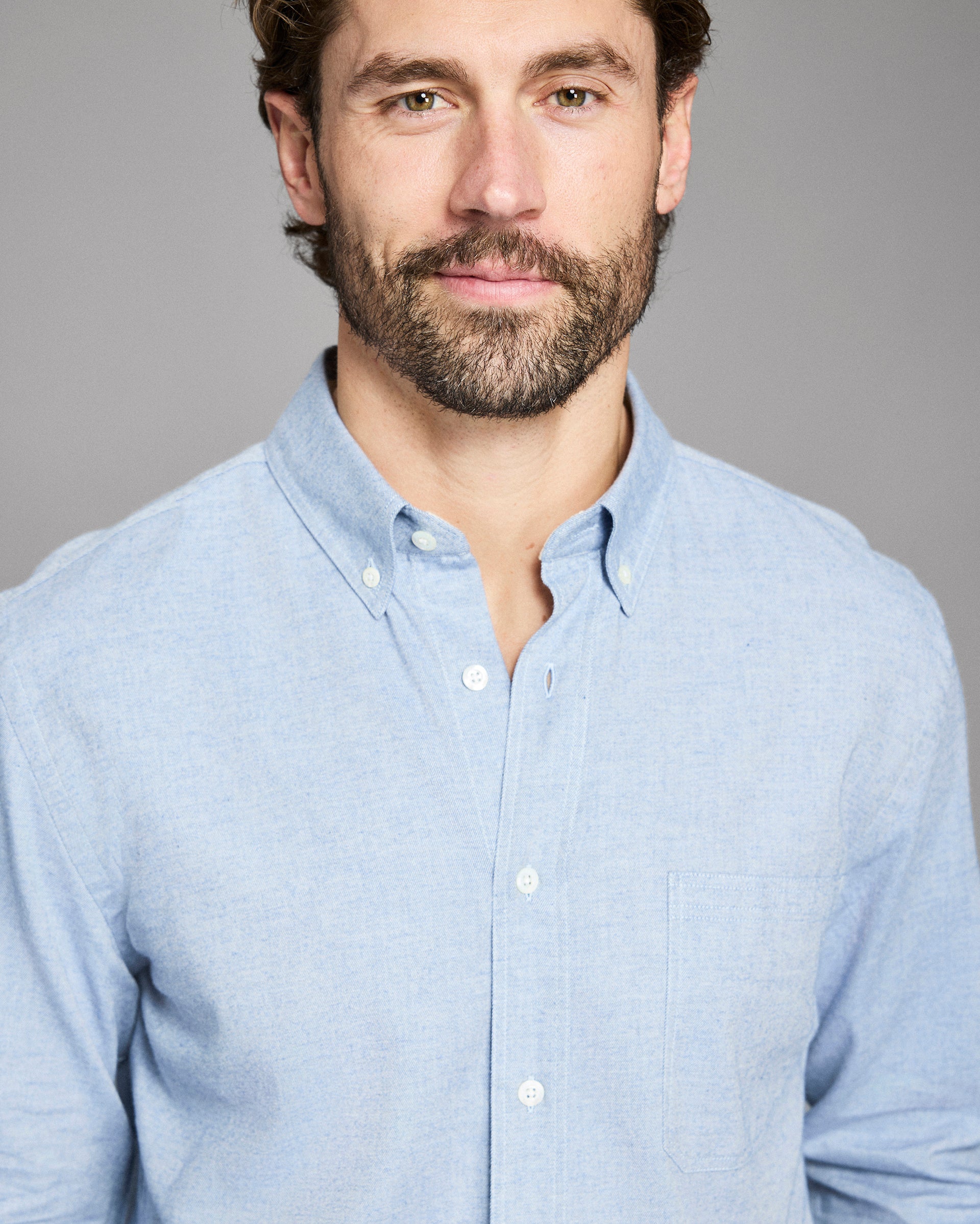 Man wearing a light blue button-up shirt against a gray background