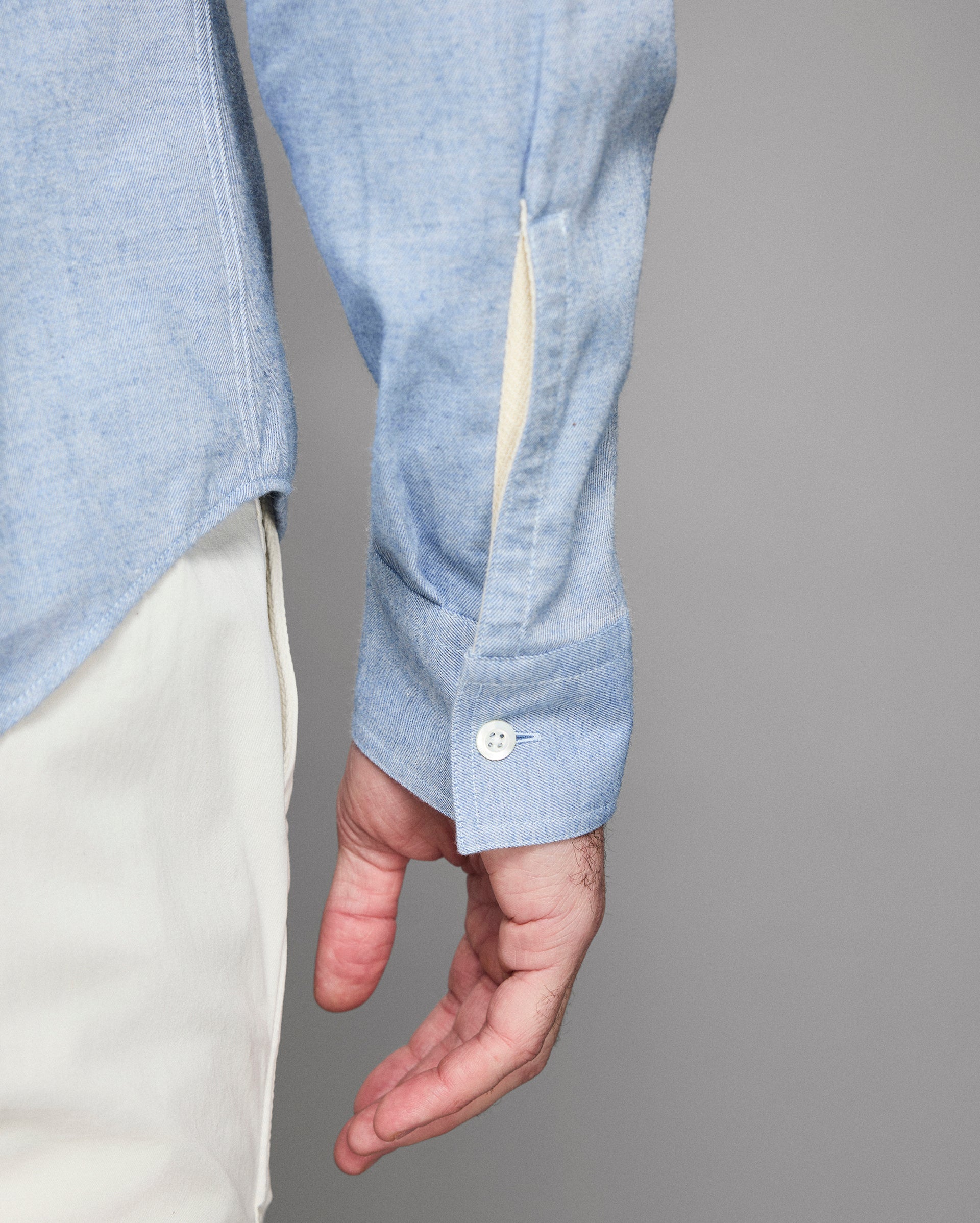 Close-up of a person wearing a light blue shirt with rolled-up sleeves against a gray background