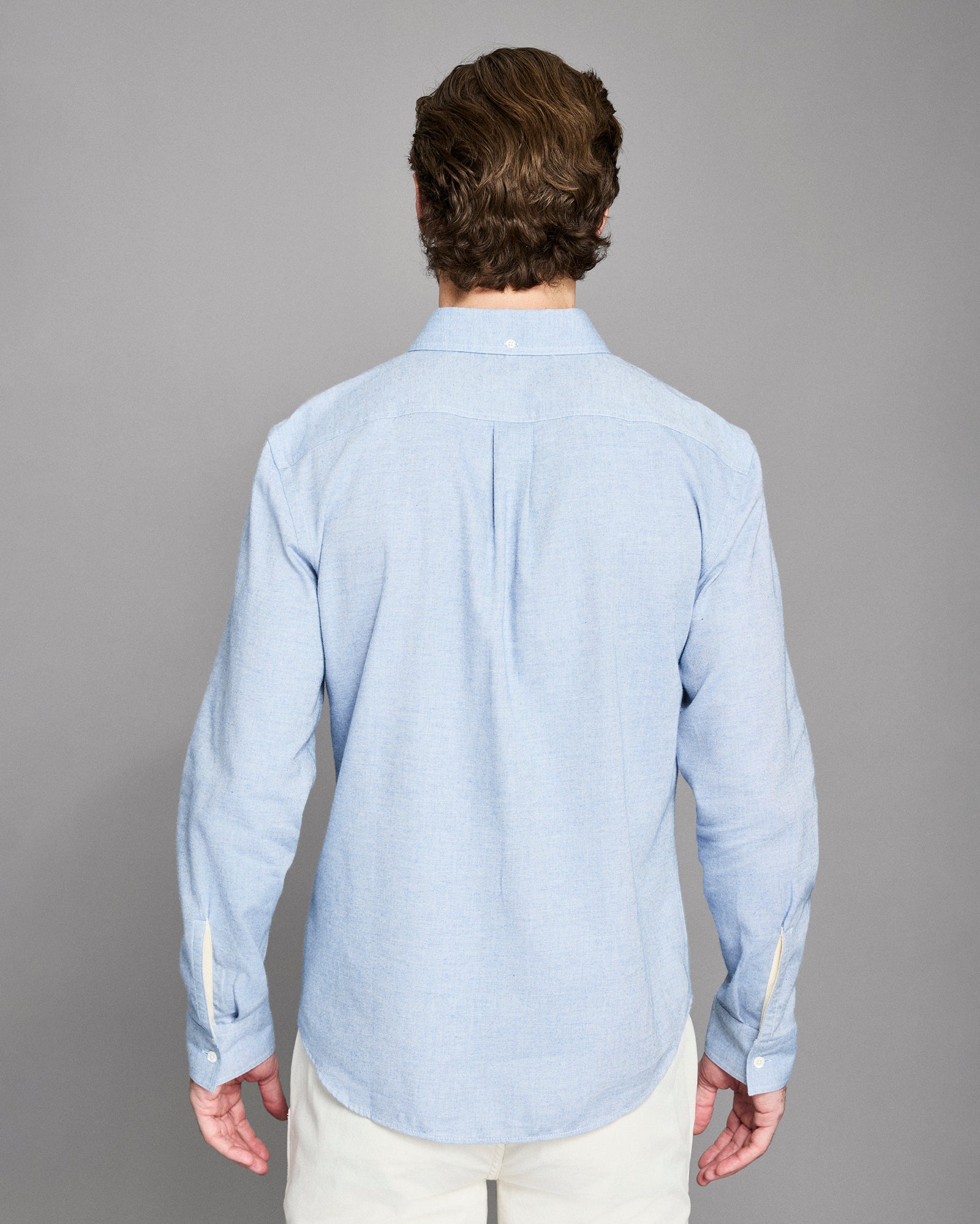 Man wearing a light blue shirt from behind on a gray background