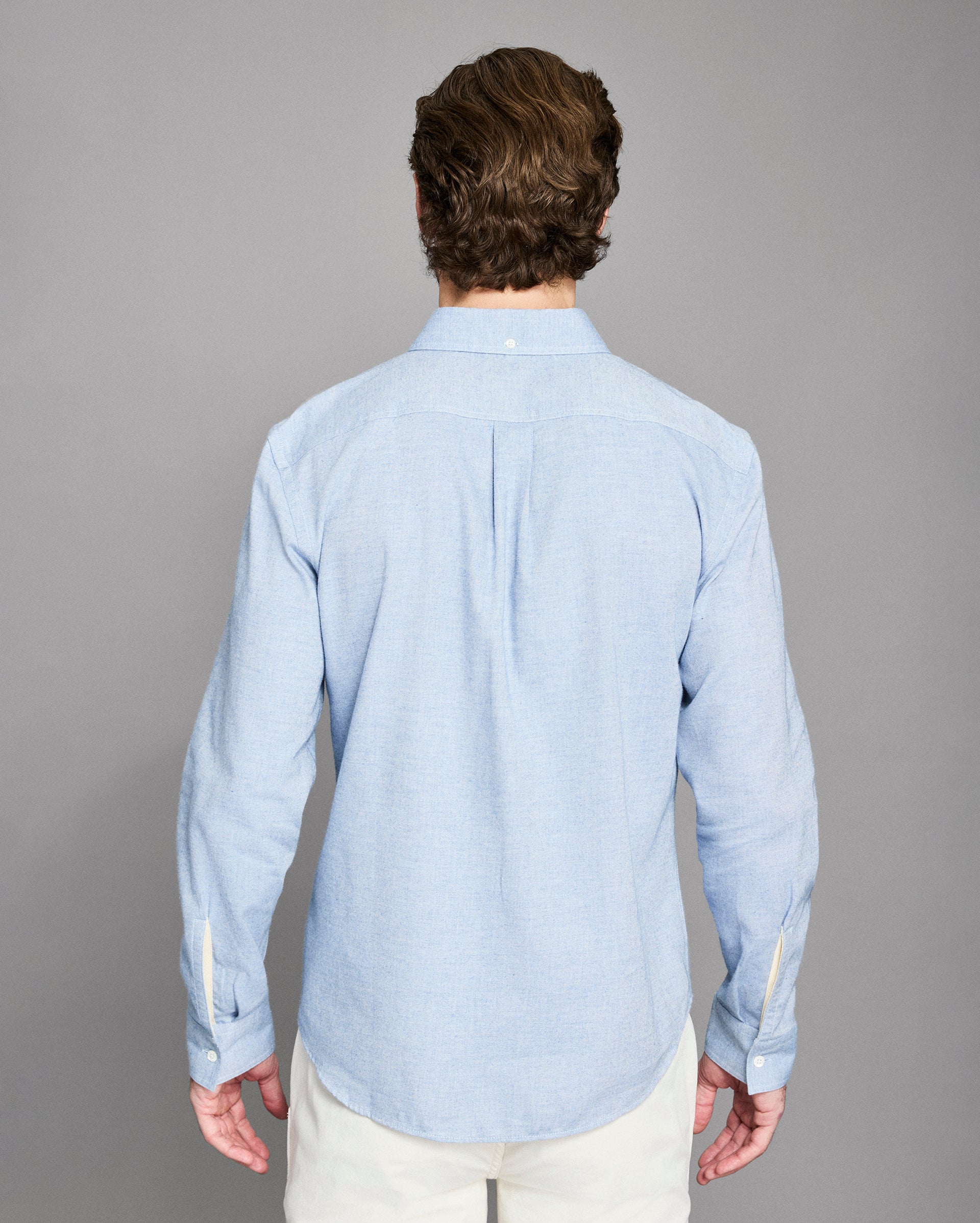 Man wearing a light blue shirt from behind on a gray background
