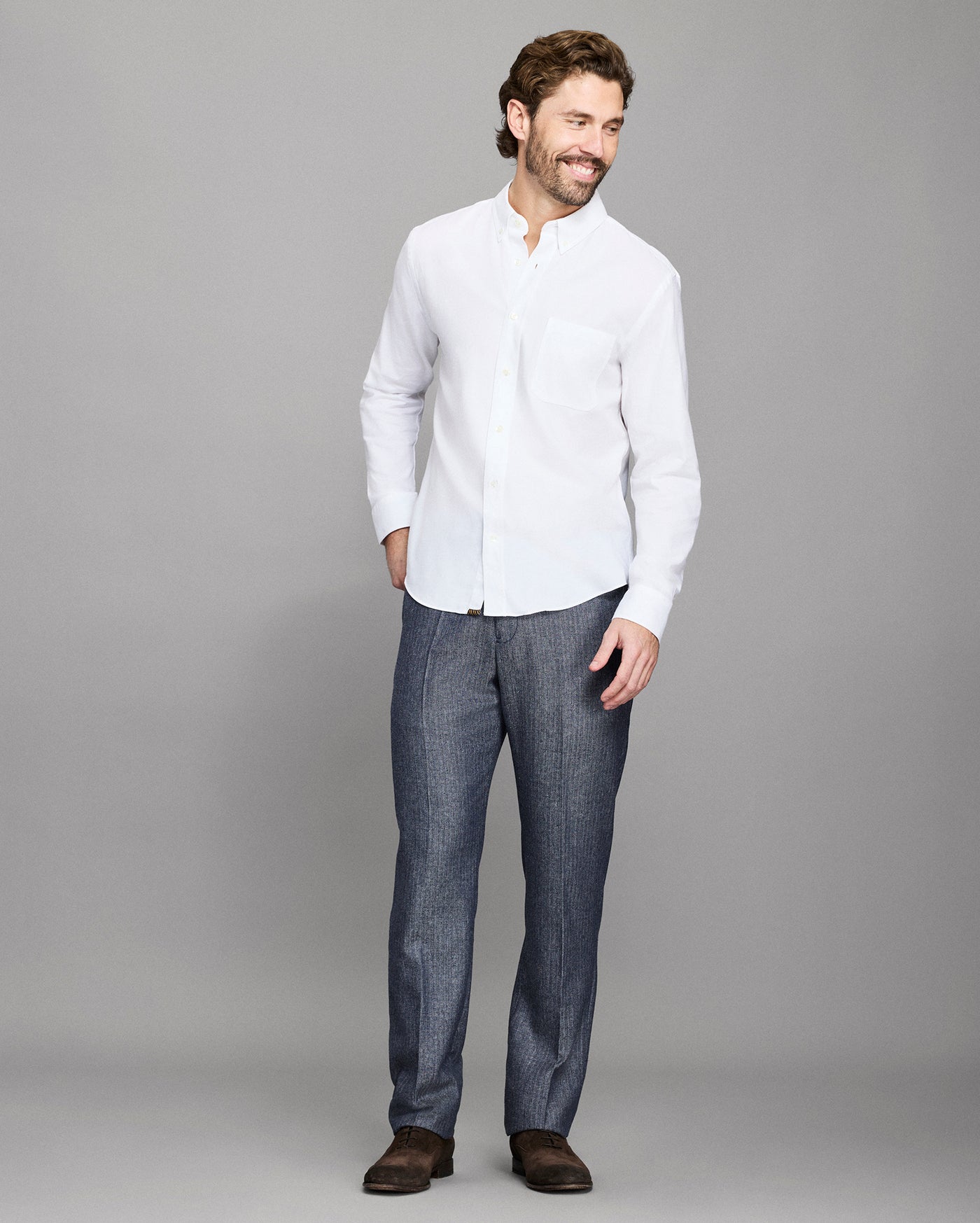 Man wearing a white shirt and dark pants against a gray background