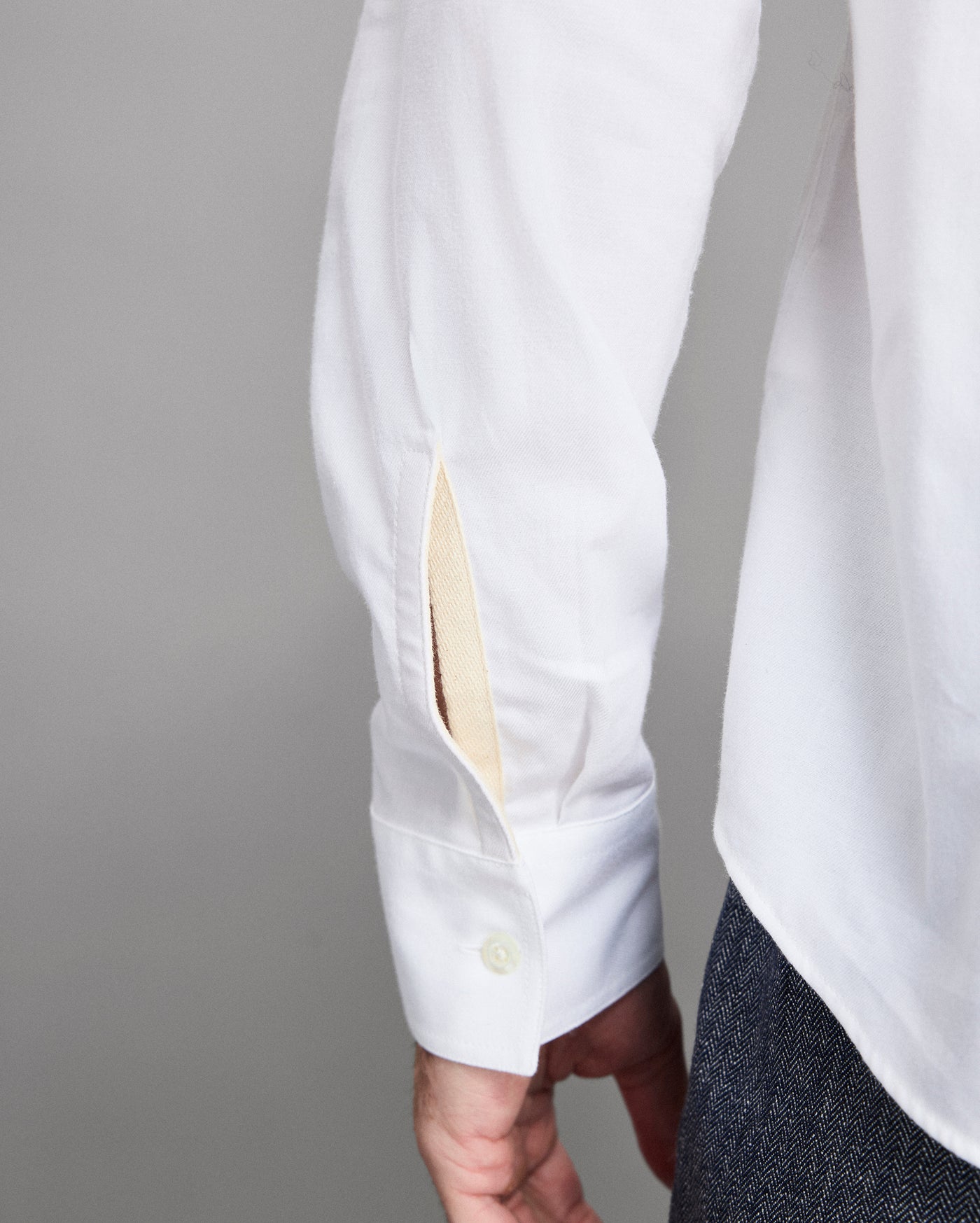 Close-up of a white shirt with a button being adjusted against a gray background