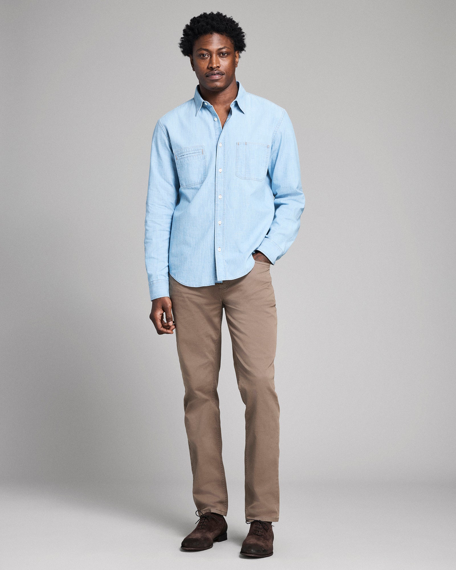 Man wearing a light blue shirt and beige pants on a gray background