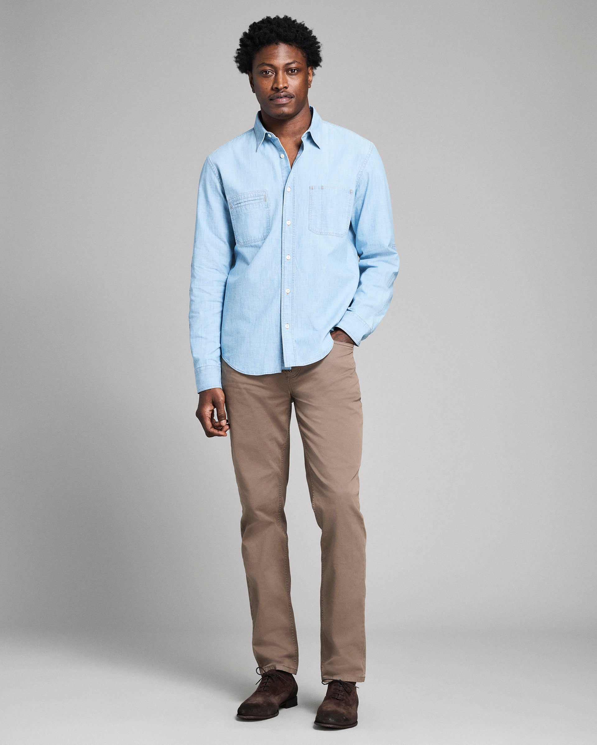 Man wearing a light blue shirt and beige pants on a gray background