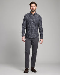 Man wearing a patterned dark shirt and gray pants on a gray background