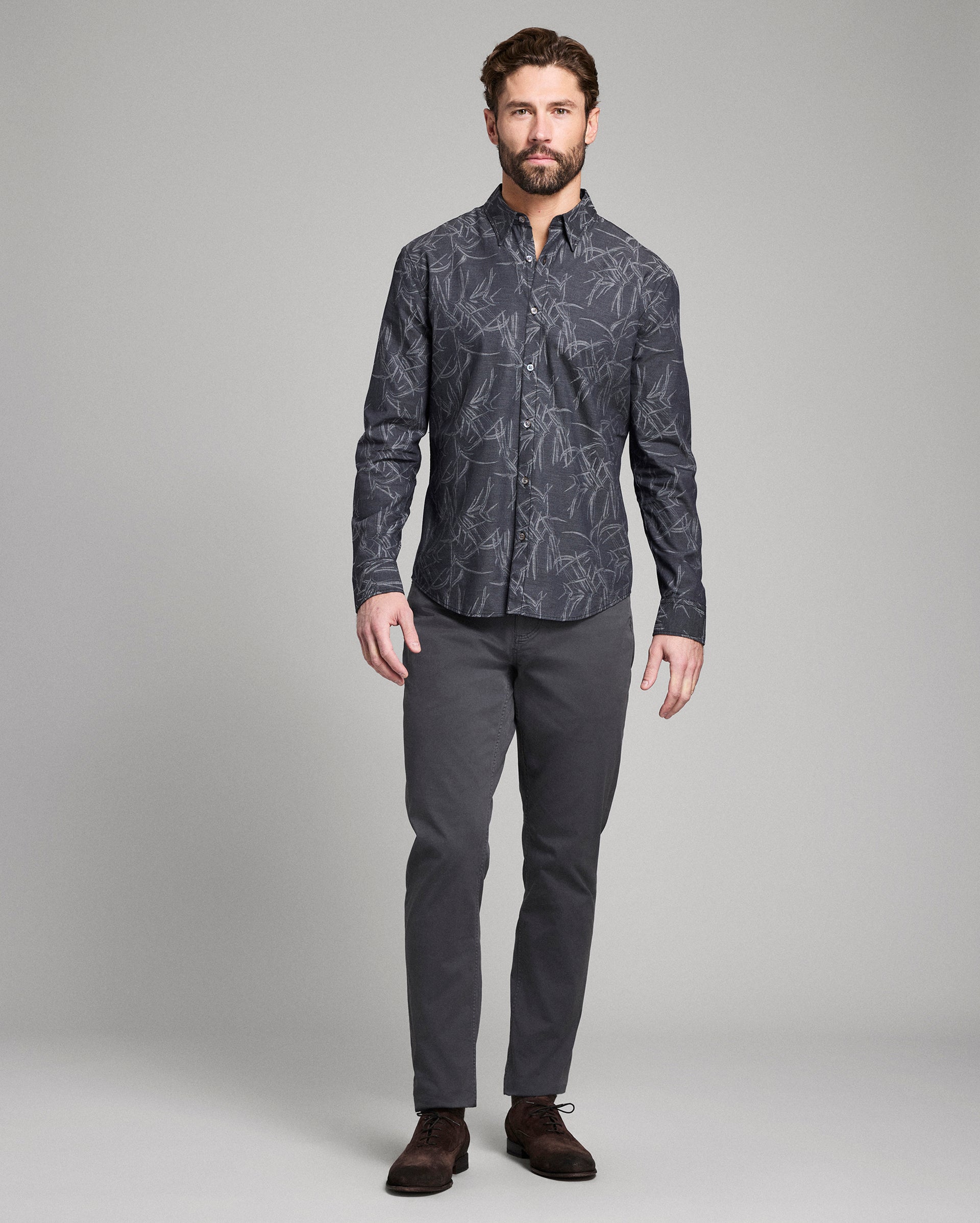 Man wearing a patterned dark shirt and gray pants on a gray background