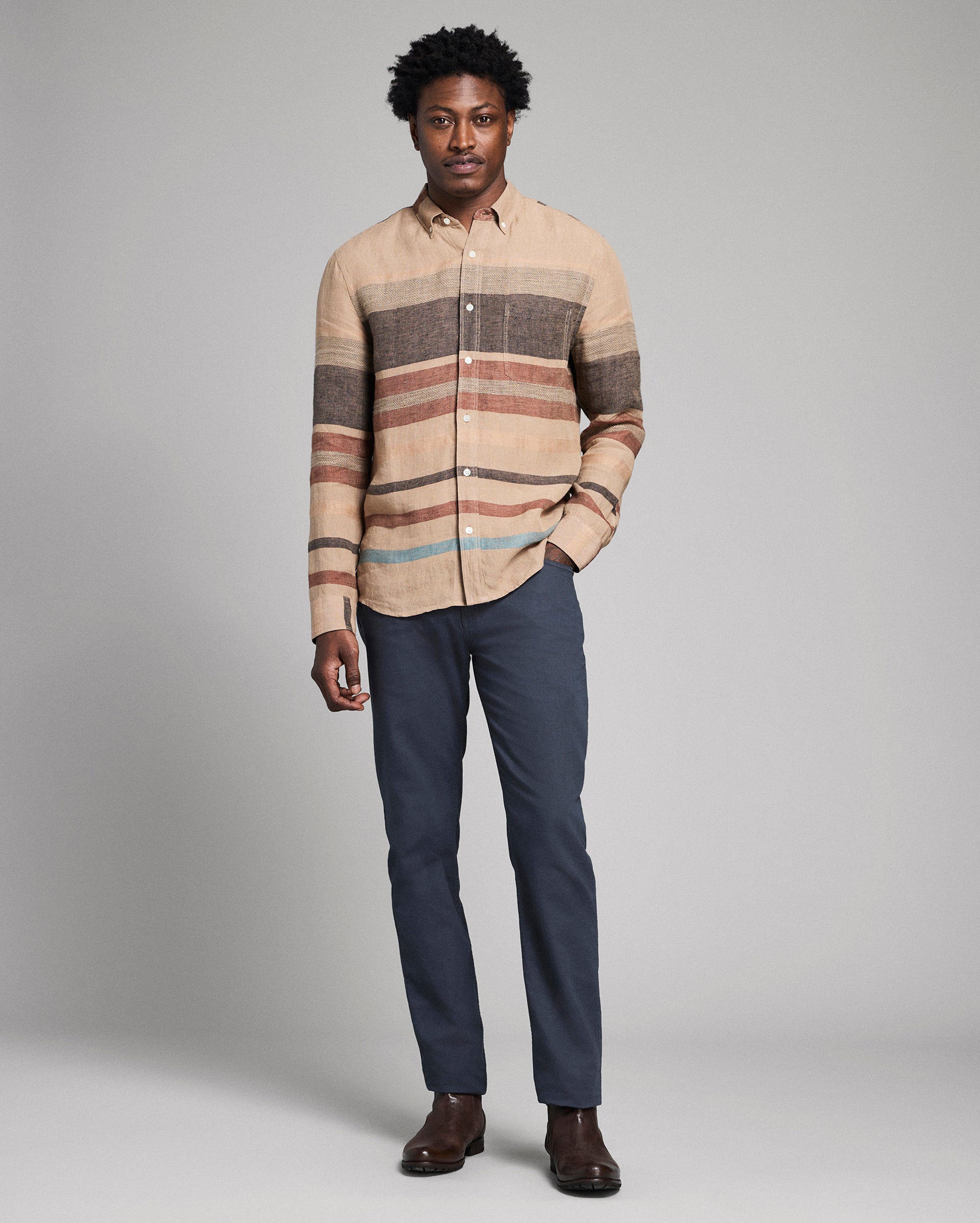 Man wearing a striped shirt and dark pants against a gray background