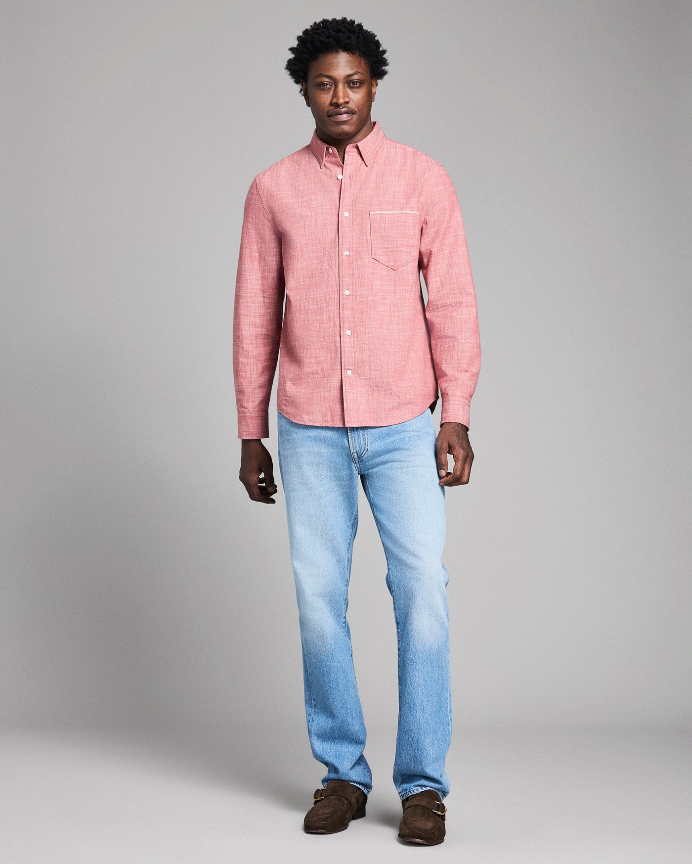 Man wearing a pink shirt and light blue jeans against a gray background