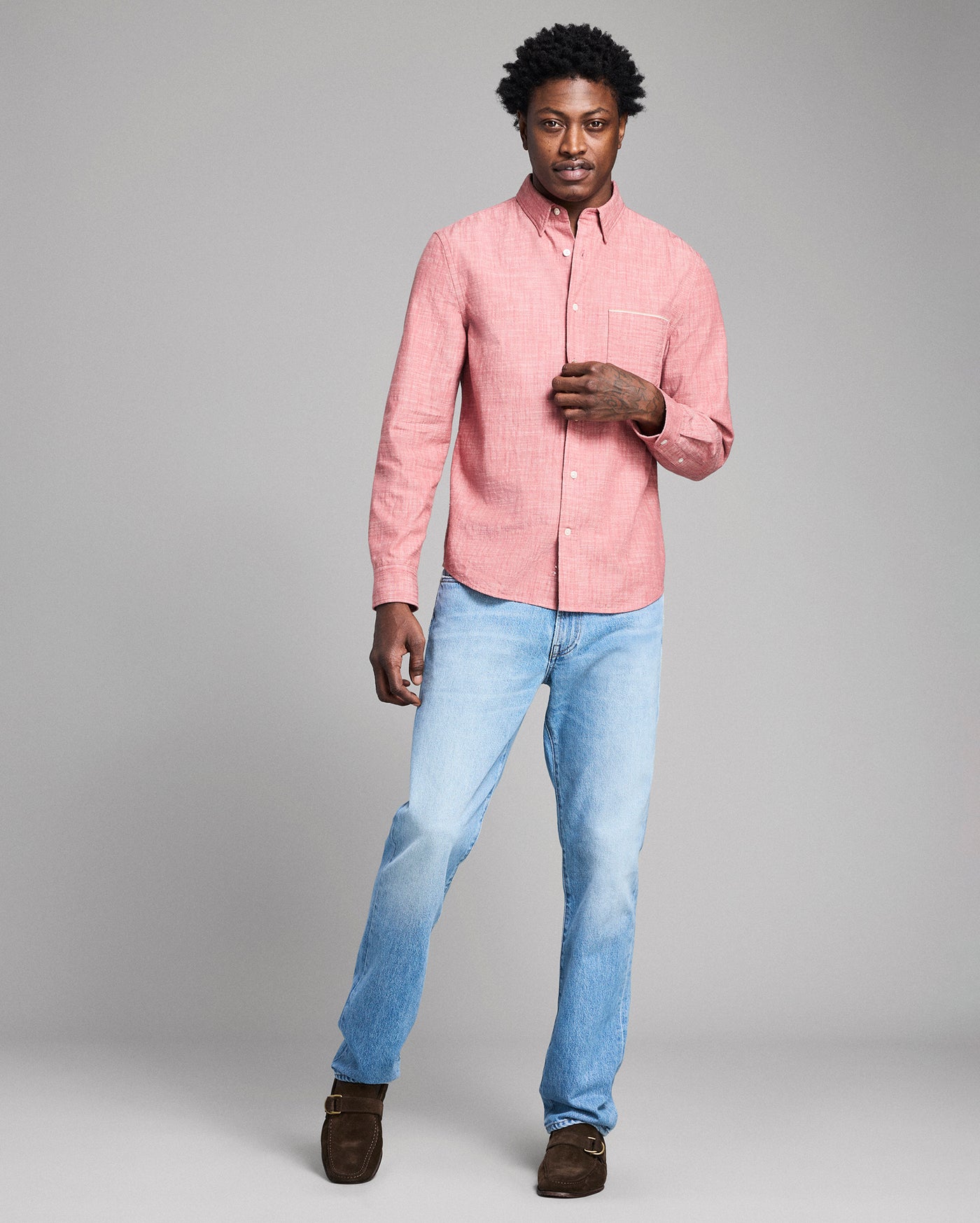 Man wearing a pink shirt and light blue jeans against a gray background