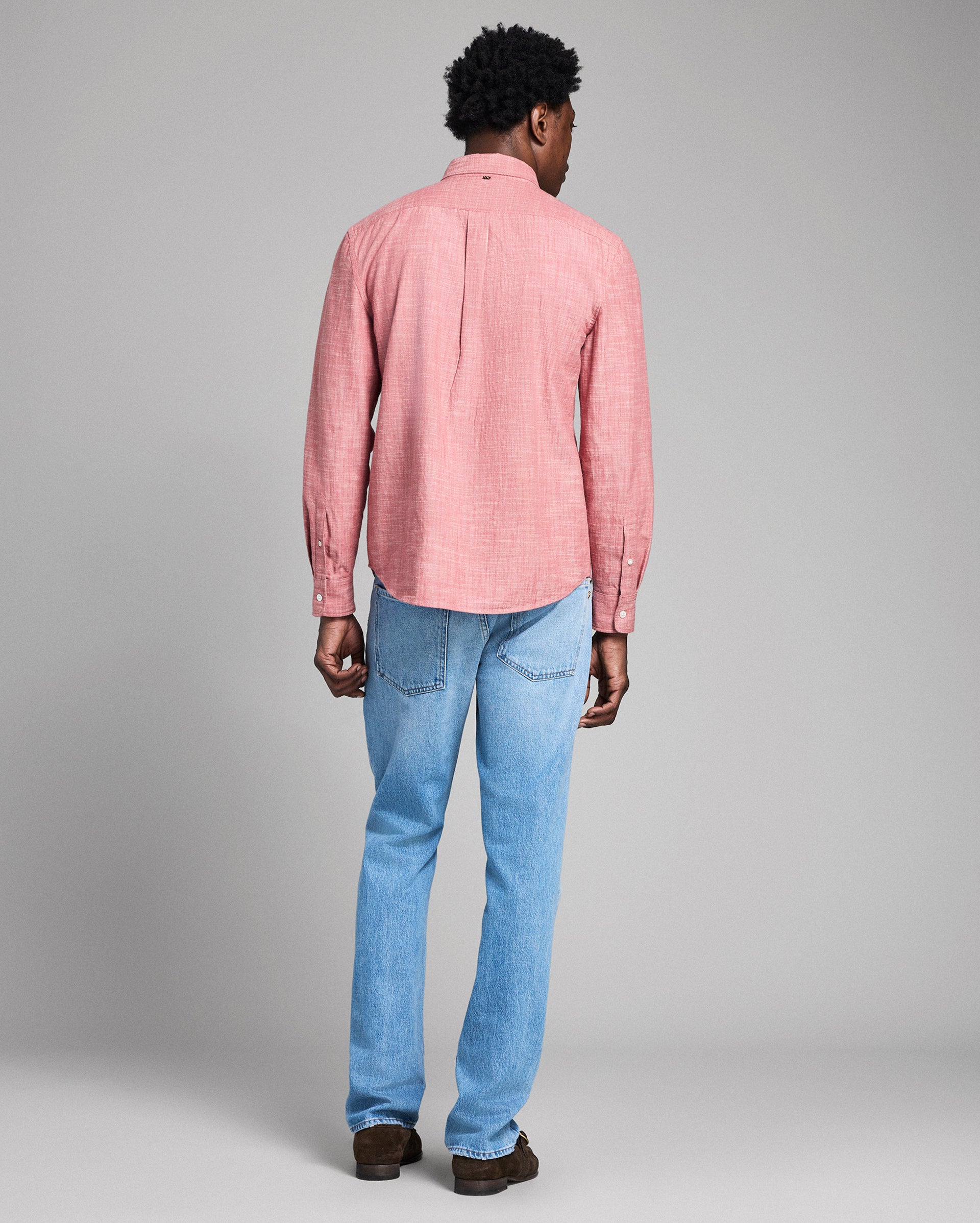 Person wearing a pink checkered shirt and blue jeans on a gray background