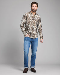 Man wearing a camouflage shirt and blue jeans on a gray background