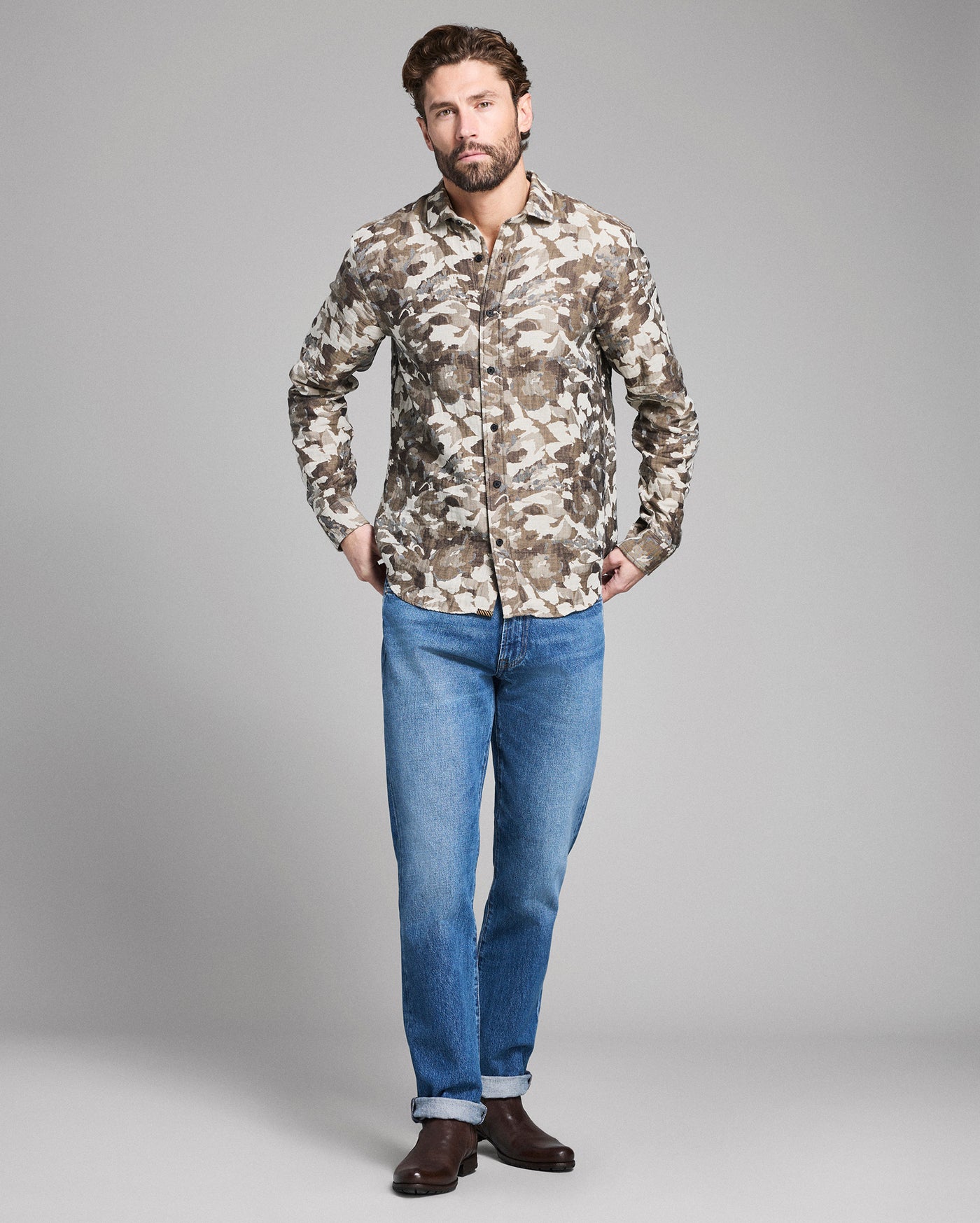 Man wearing a camouflage shirt and blue jeans on a gray background