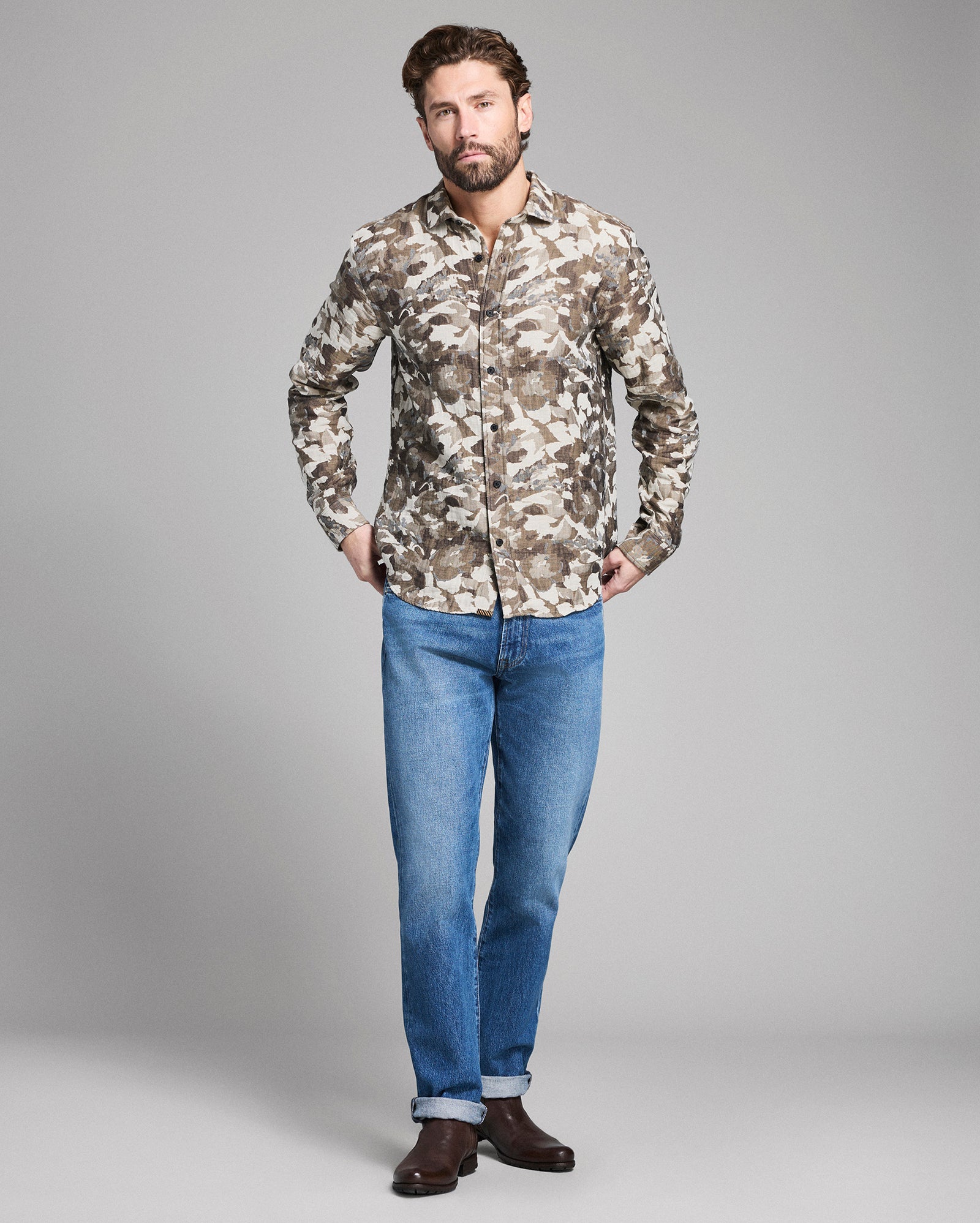 Man wearing a camouflage shirt and blue jeans on a gray background