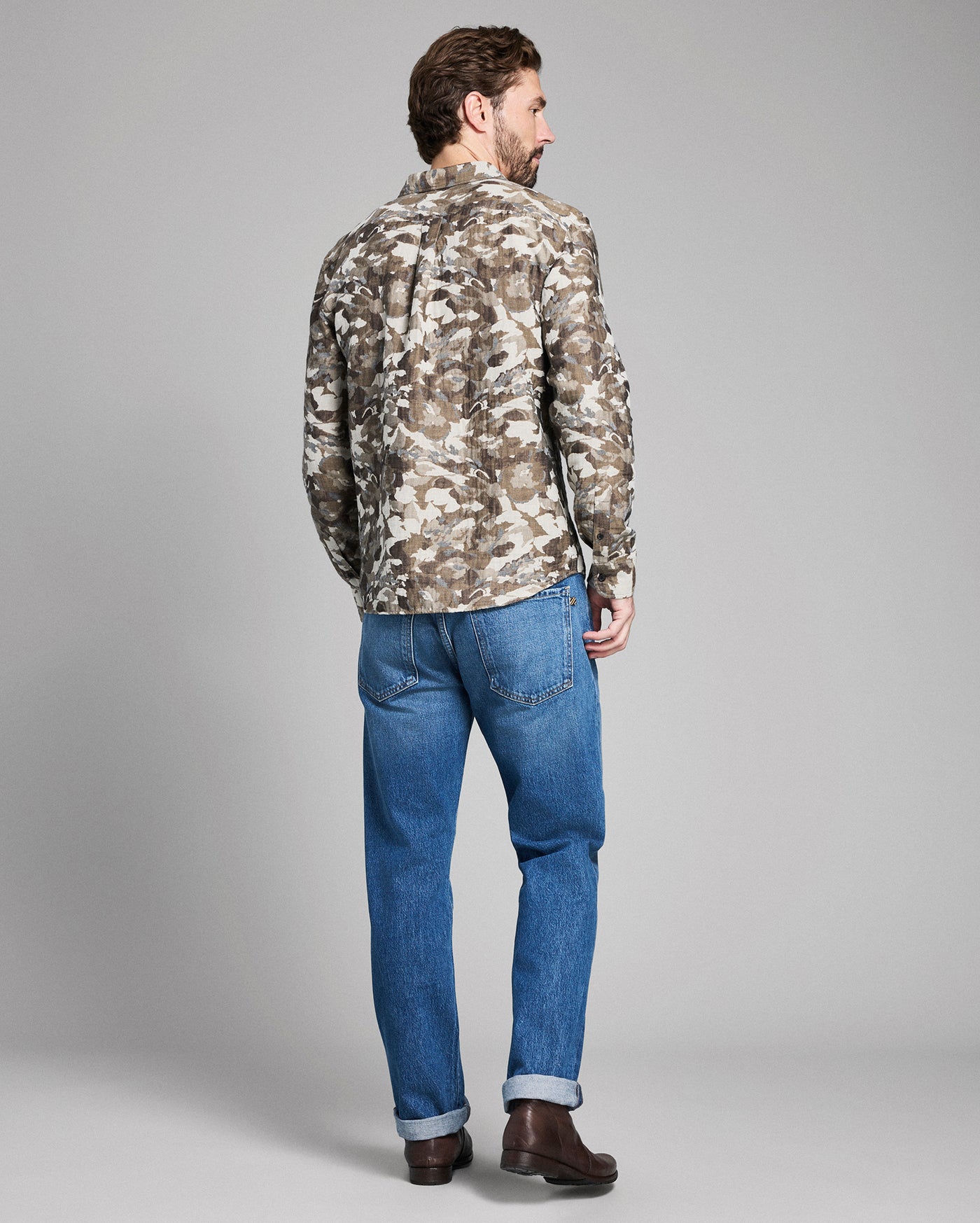 Man wearing a camouflage jacket and blue jeans on a gray background