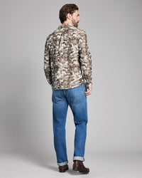 Man wearing a camouflage jacket and blue jeans on a gray background