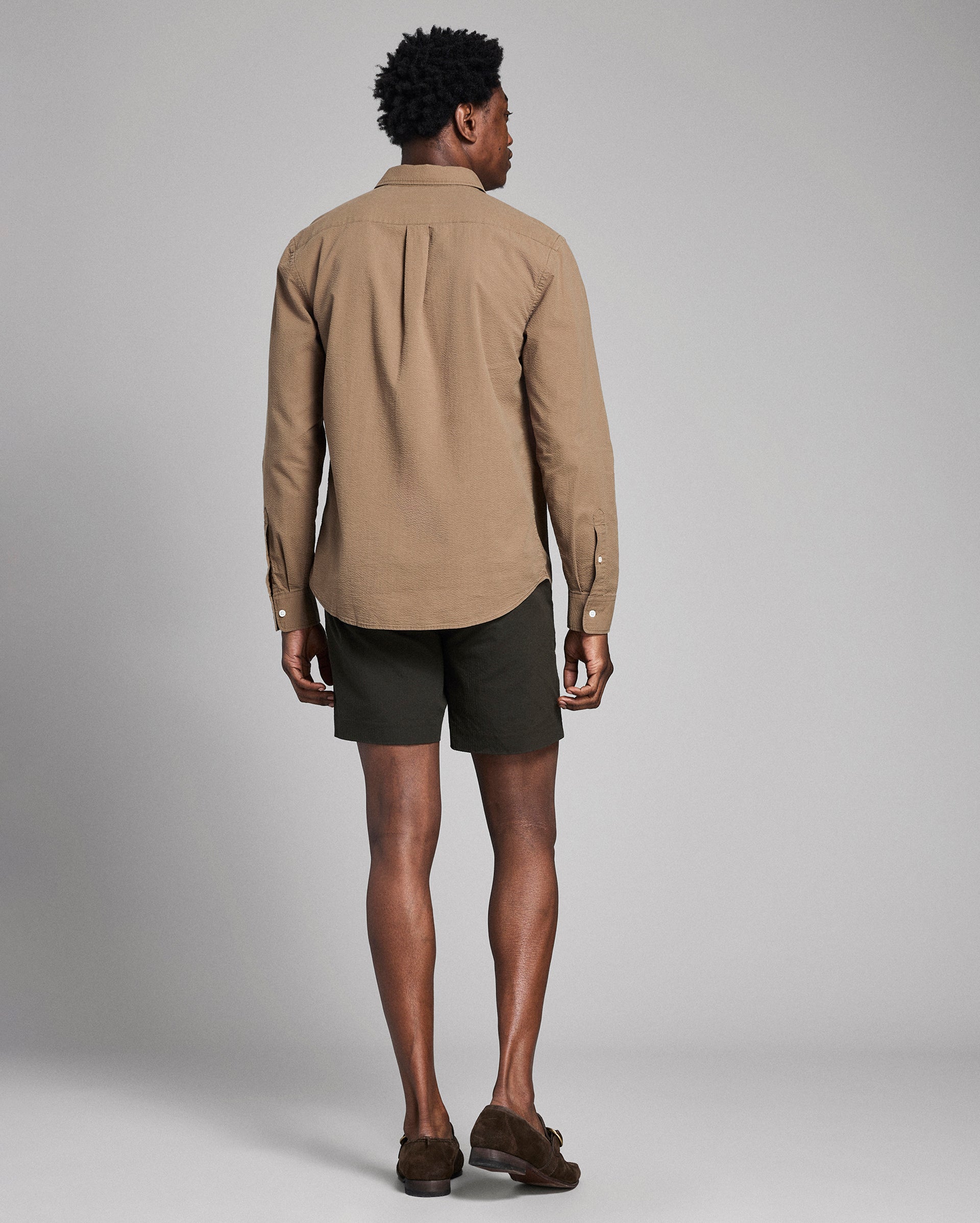 Man wearing a beige shirt and dark shorts against a gray background