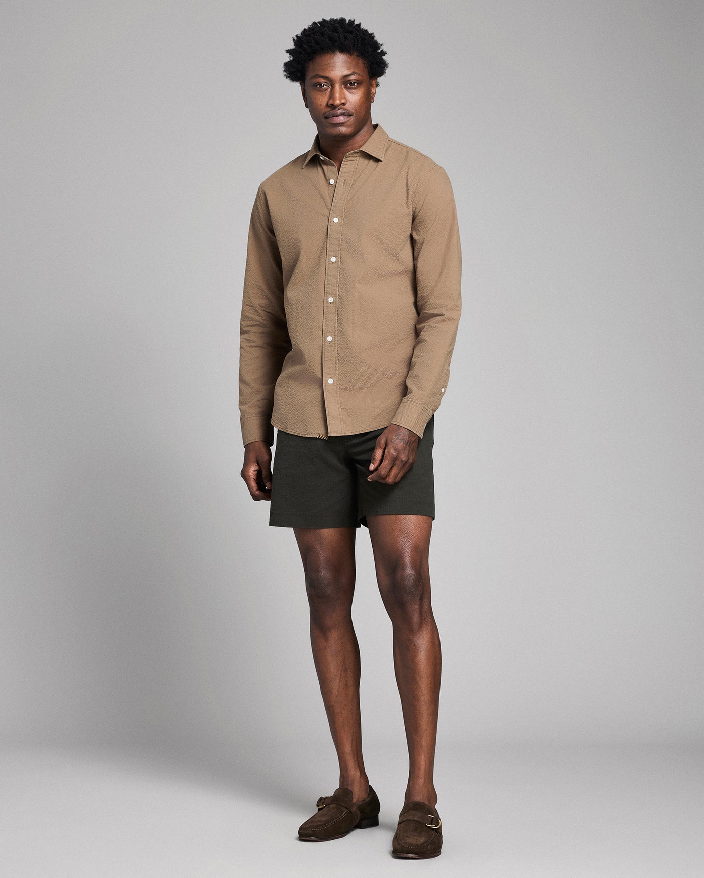 Man wearing a beige shirt and green shorts against a plain background
