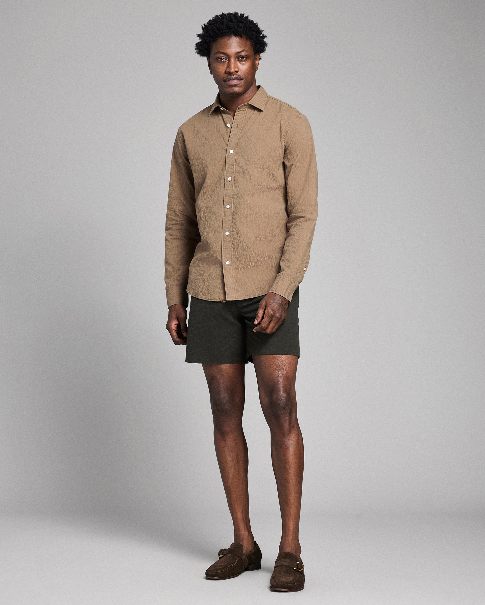 Man wearing a beige shirt and green shorts against a plain background