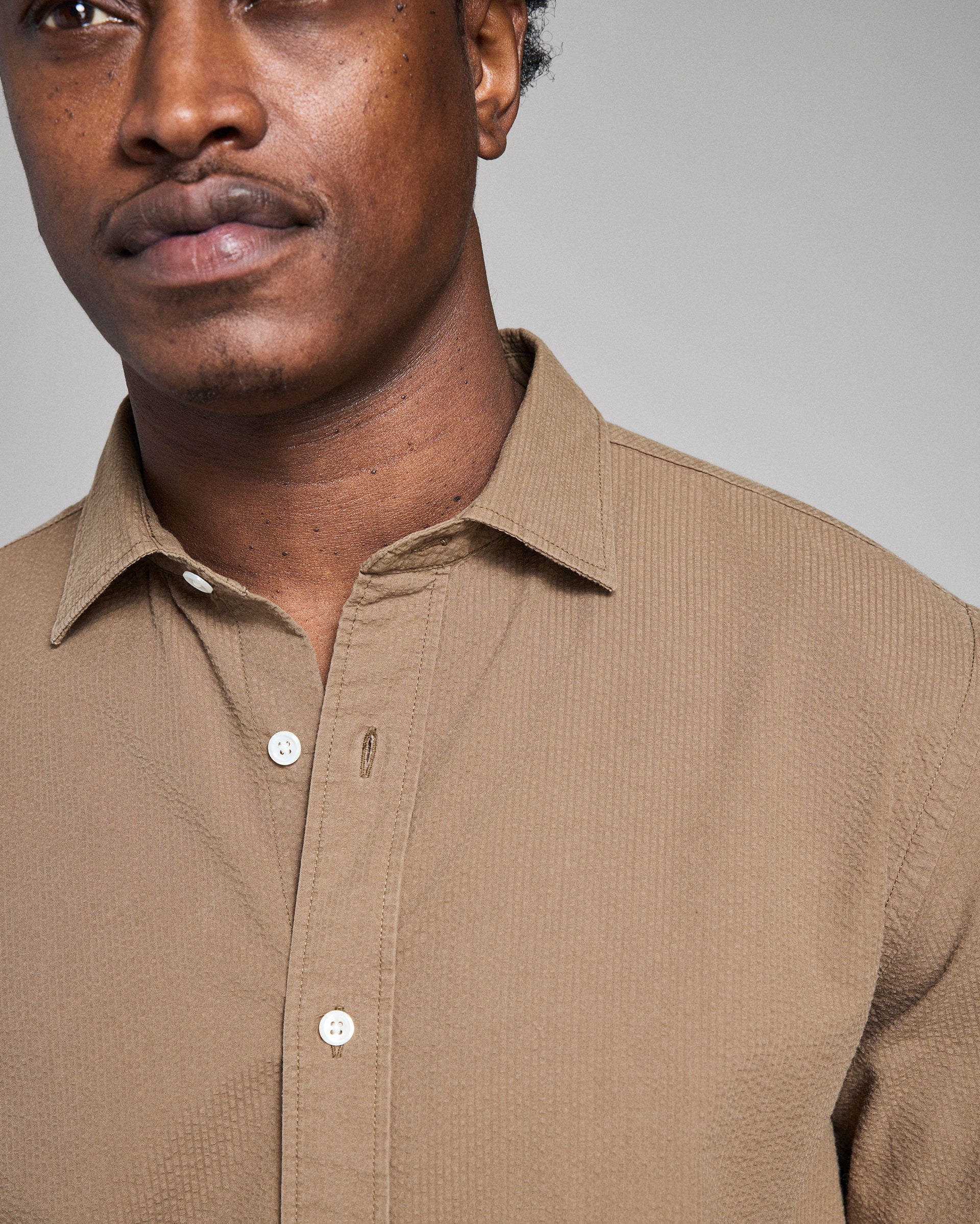 Man wearing a brown button-up shirt against a gray background