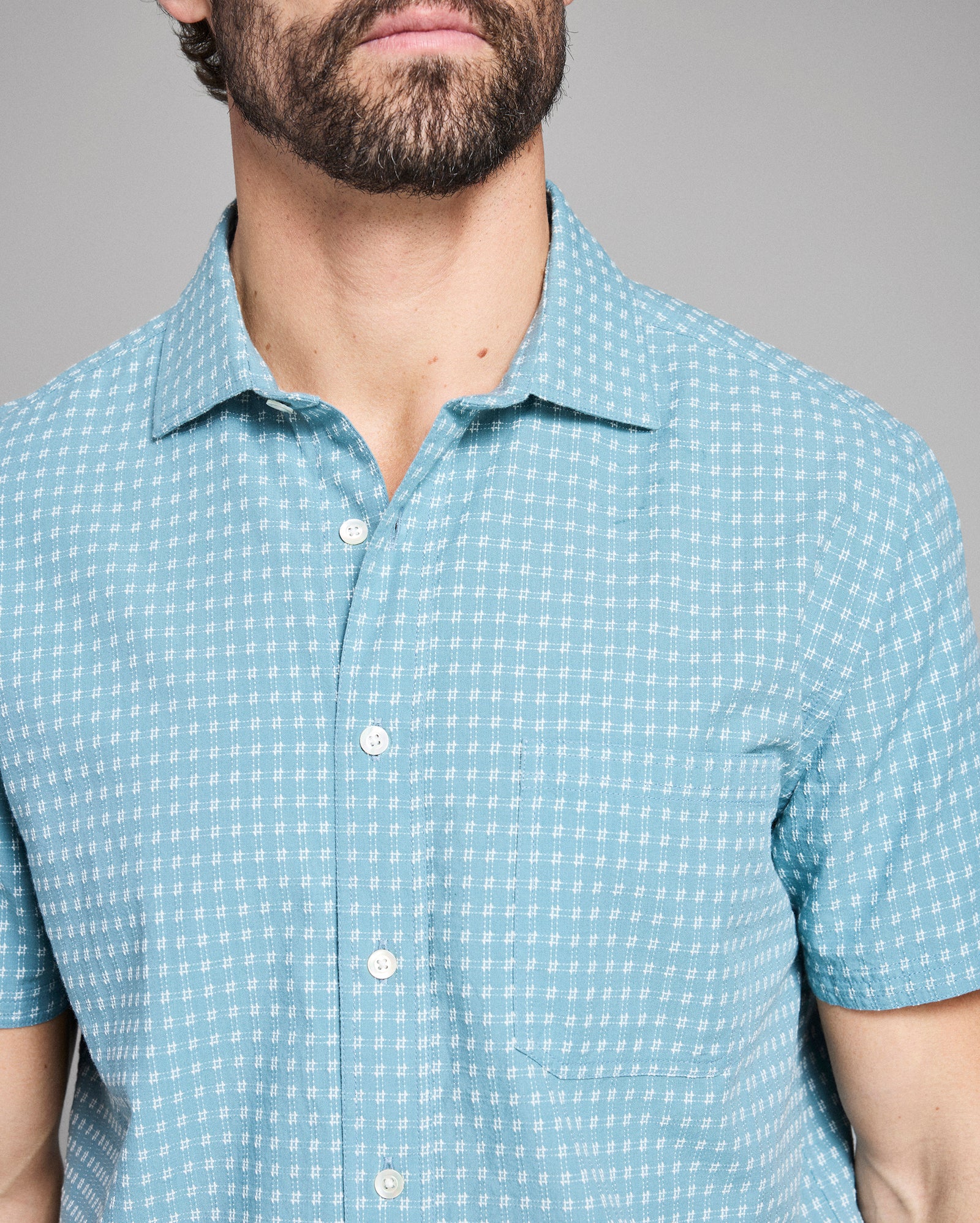 Man wearing a light blue checkered shirt against a gray background