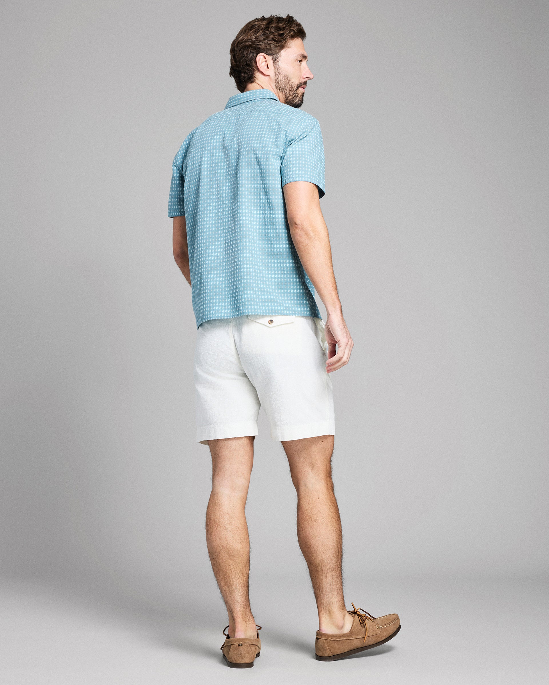 Man wearing a light blue checkered shirt and white shorts on a gray background