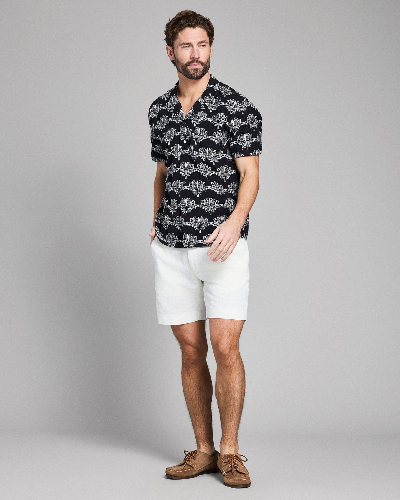 Man wearing a black patterned shirt and white shorts on a gray background