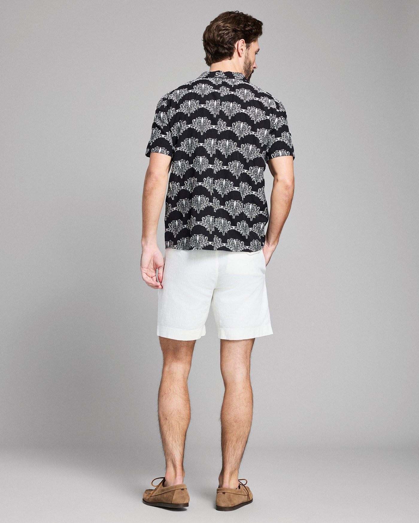 Man wearing a black patterned shirt and white shorts on a gray background