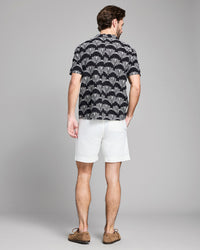 Man wearing a black patterned shirt and white shorts on a gray background