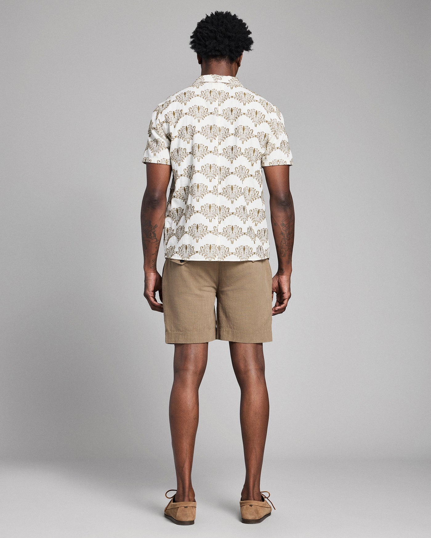 Man wearing a patterned shirt and beige shorts on a gray background