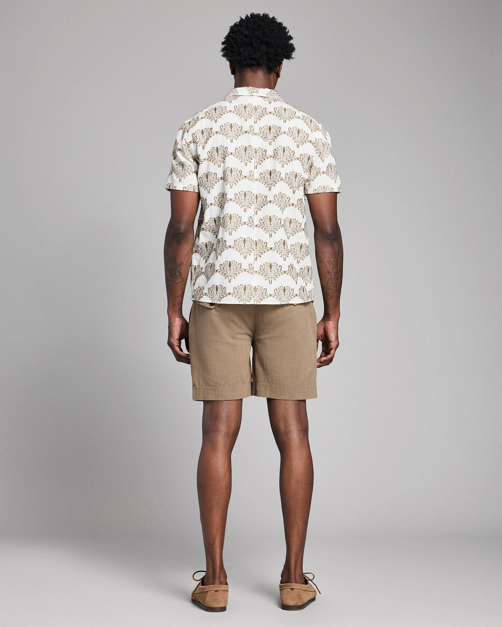 Man wearing a patterned shirt and beige shorts on a gray background