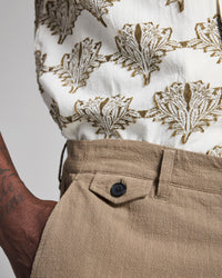 Close-up of a person wearing a white shirt with brown leaf pattern and beige pants.