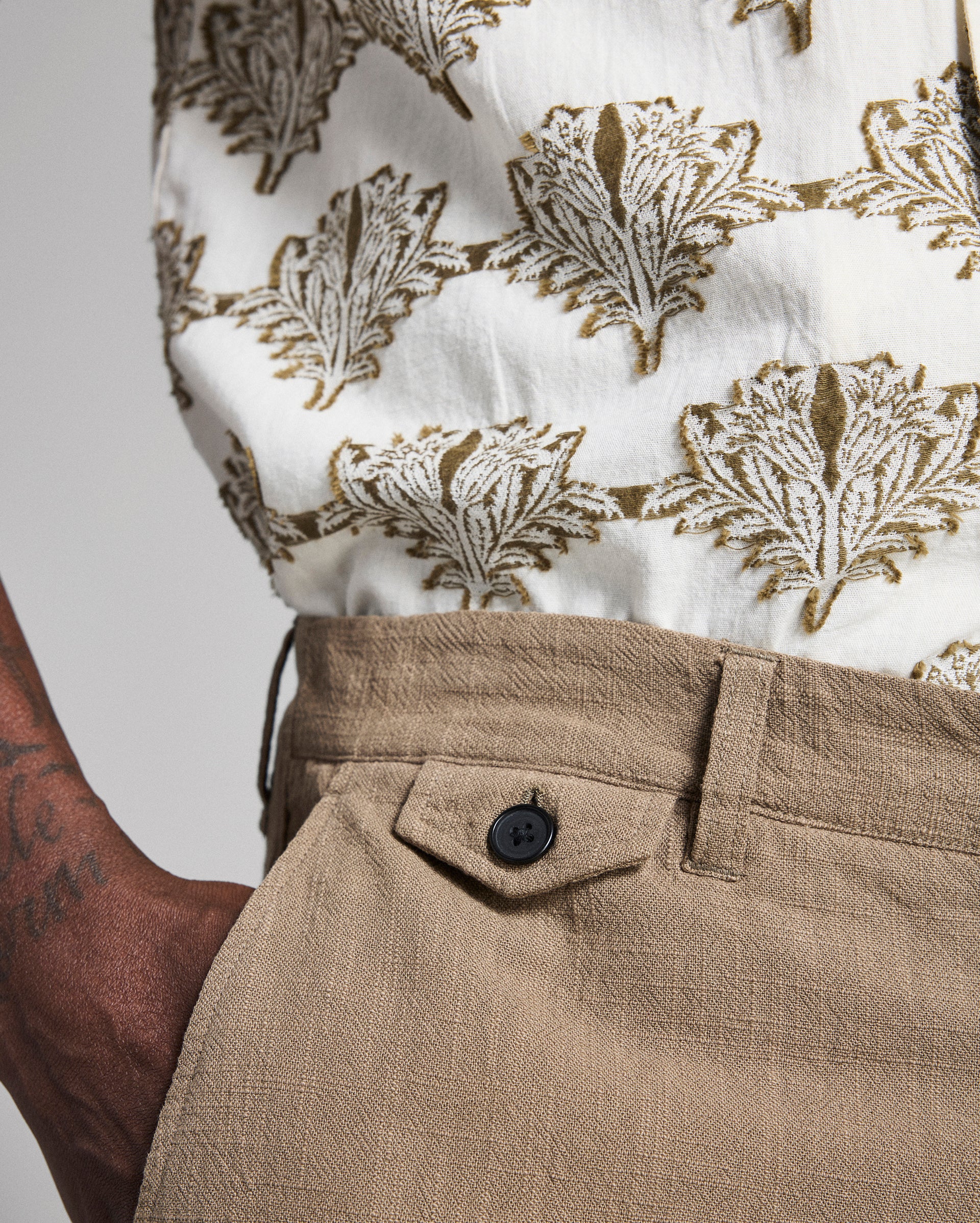 Close-up of a person wearing a white shirt with brown leaf pattern and beige pants.