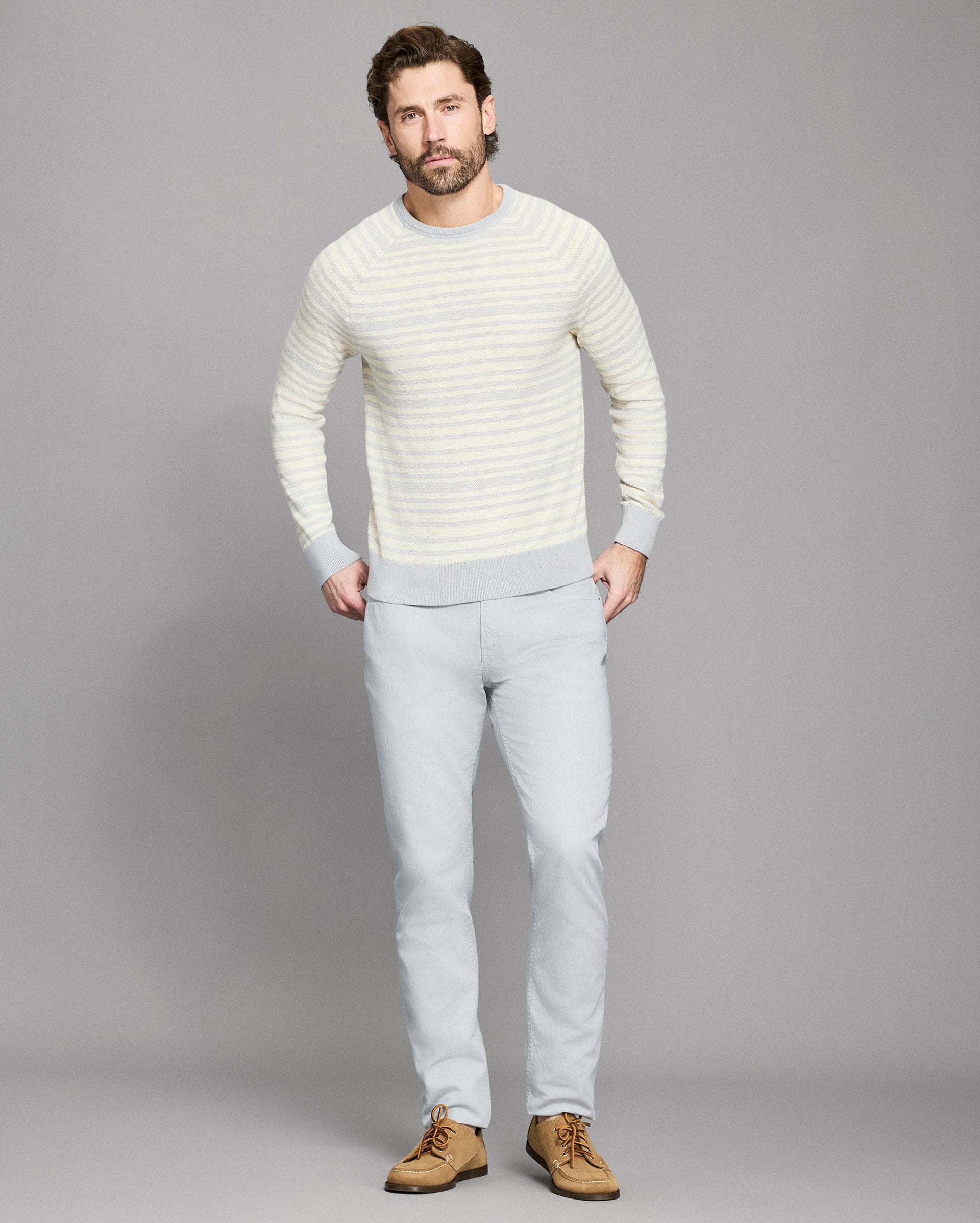 Man wearing a light gray sweater and pants against a gray background
