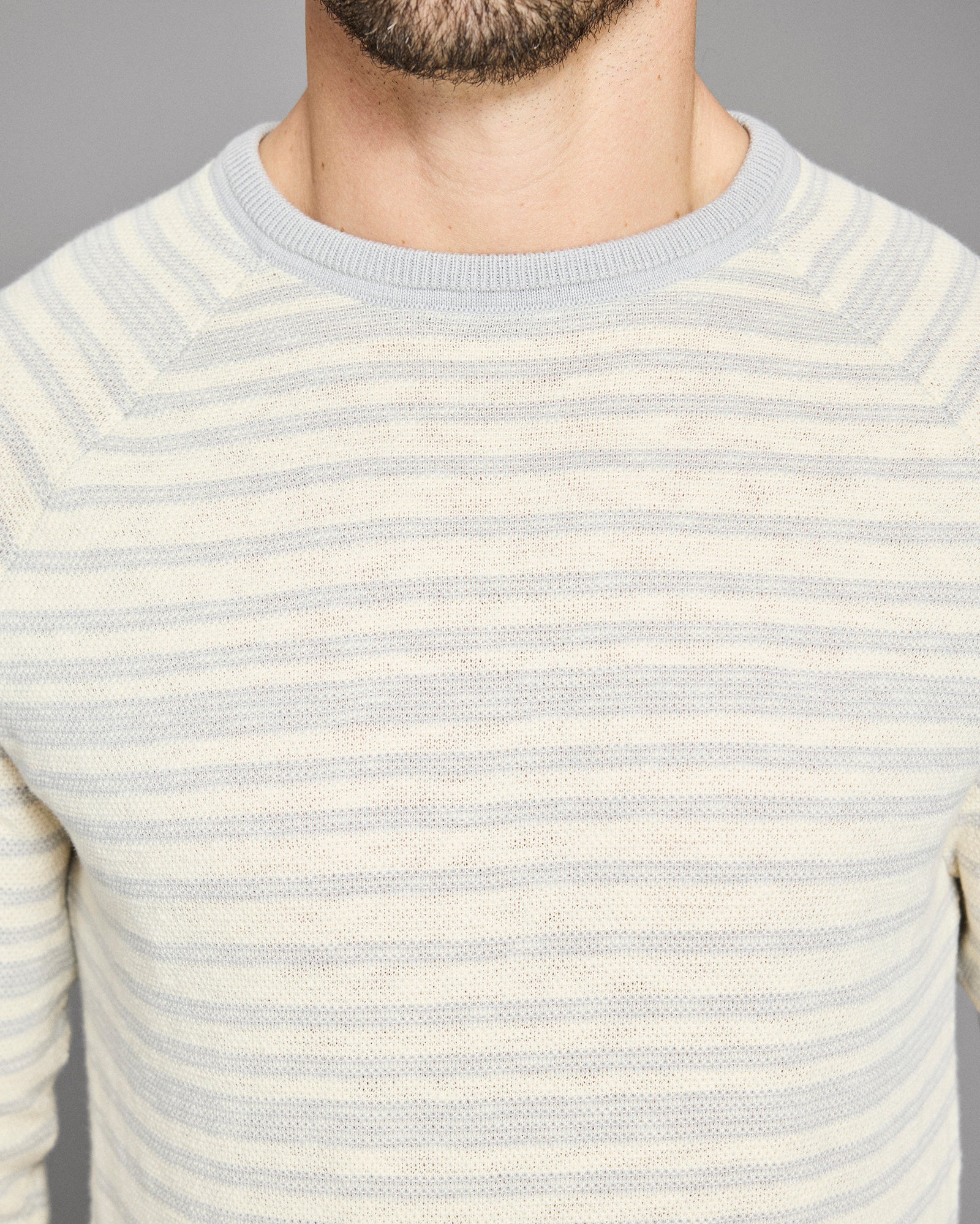 Close-up of a person wearing a light blue and white striped sweater against a gray background