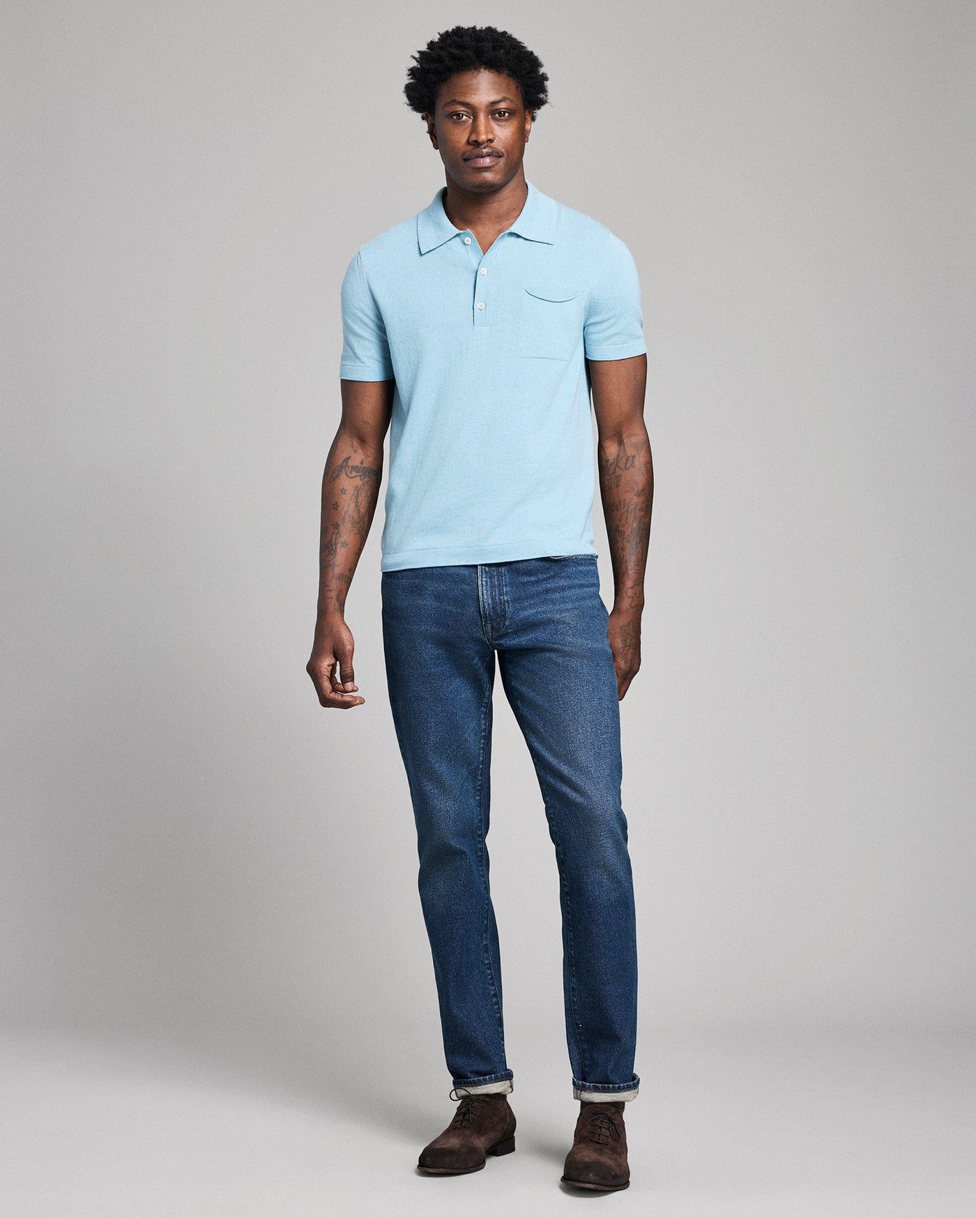 Man wearing a light blue polo shirt and dark blue jeans against a plain background
