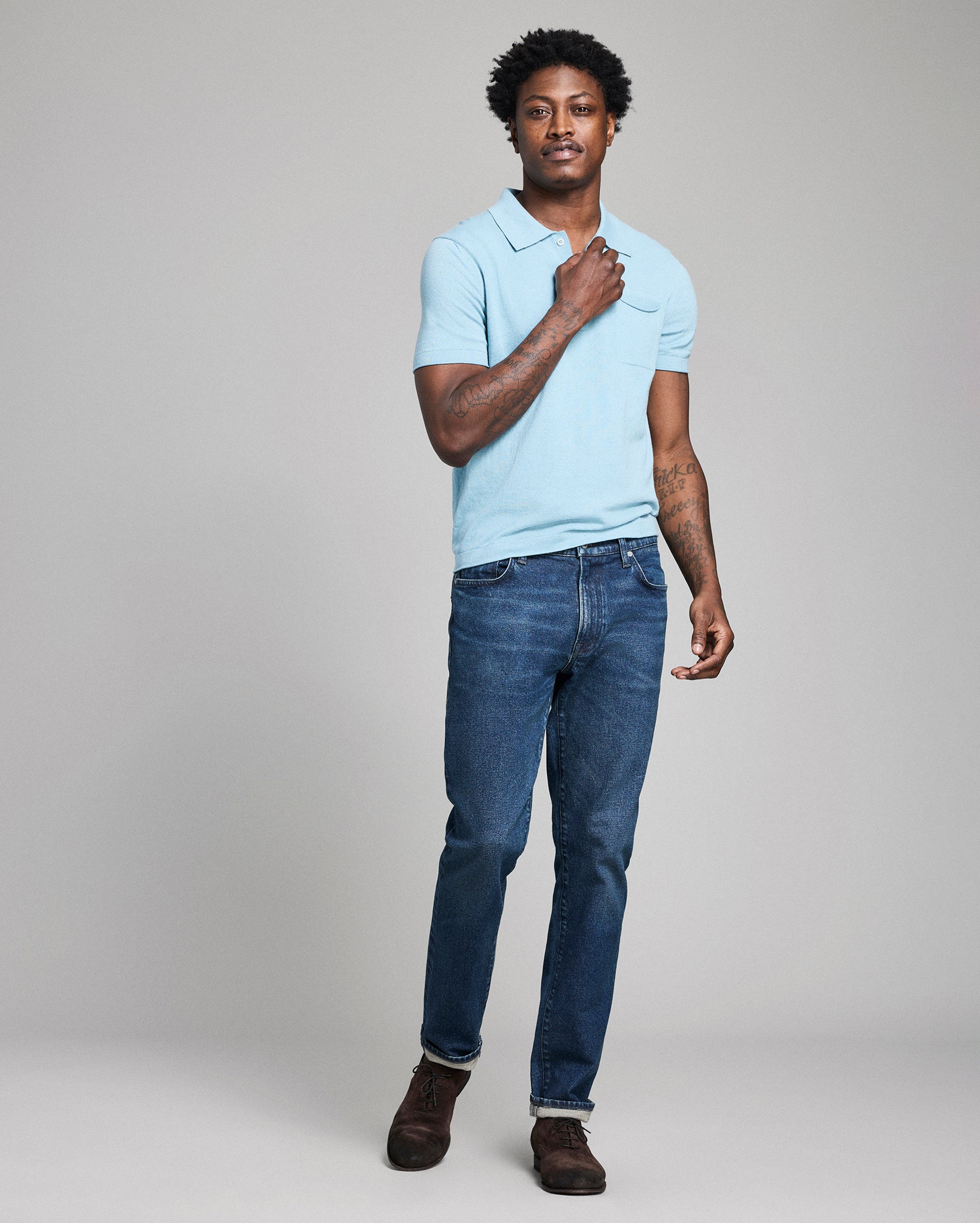 Man wearing a light blue polo shirt and dark blue jeans on a gray background