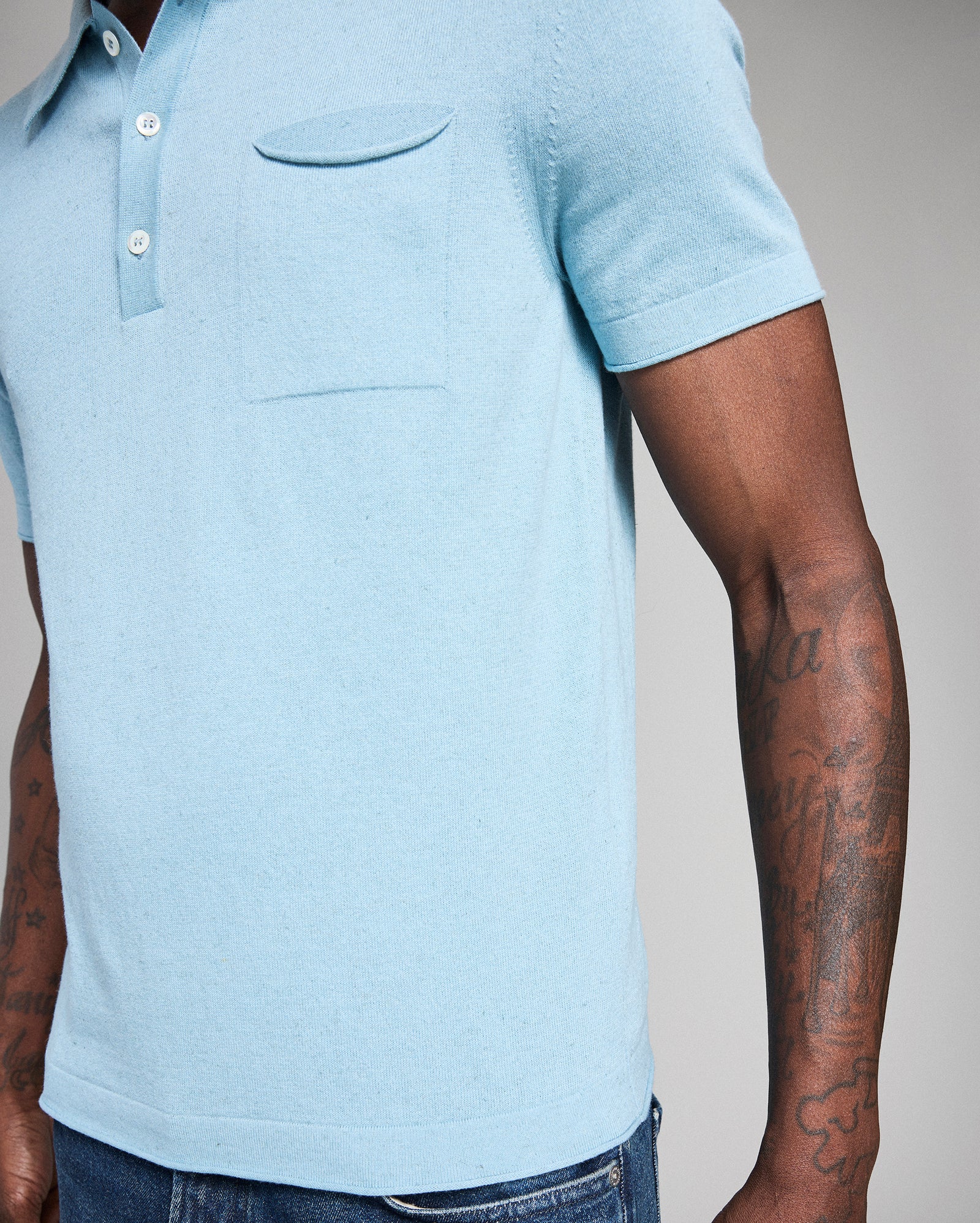 Light blue polo shirt worn by a person with tattoos on arms against a neutral background