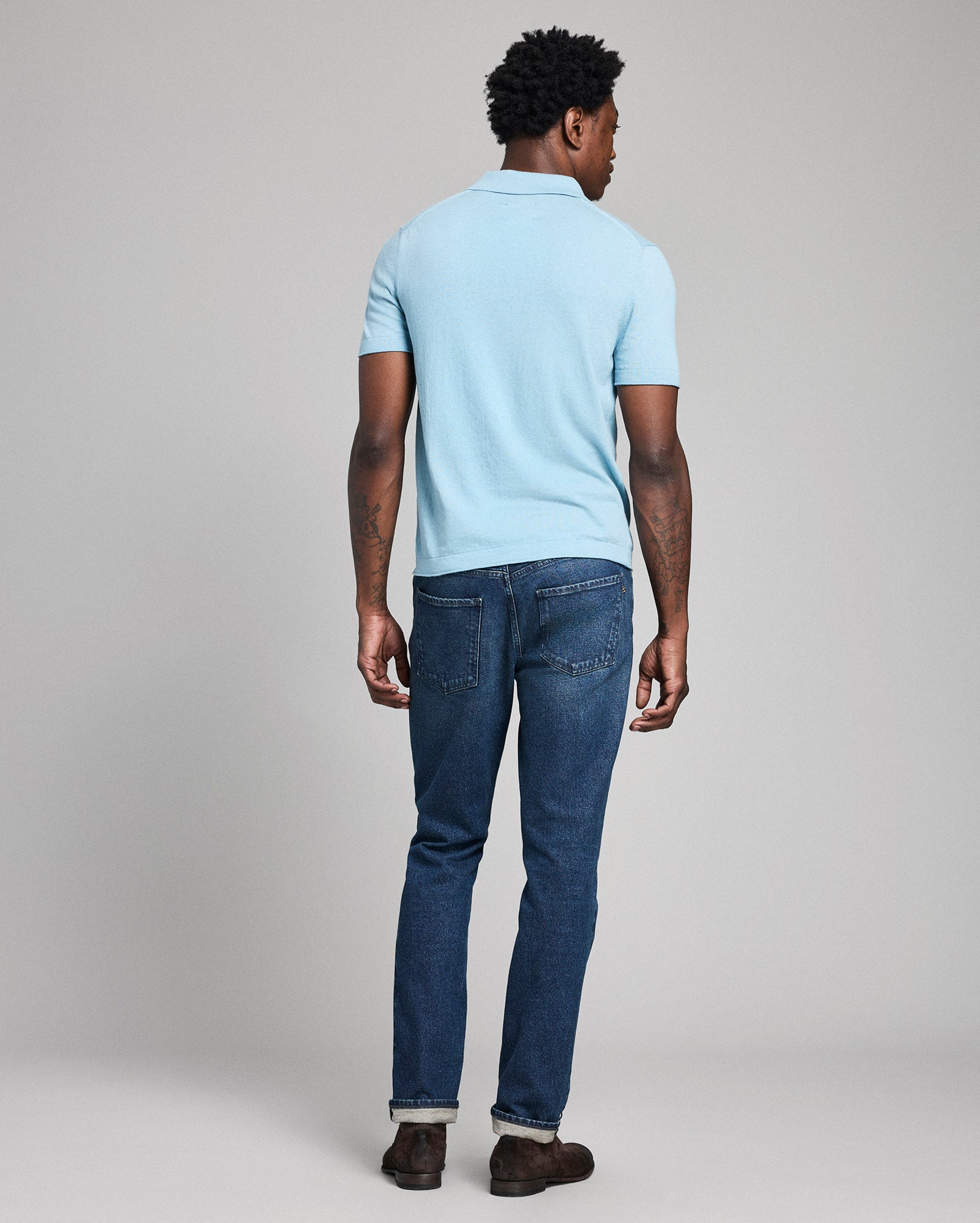 Man wearing a light blue polo shirt and dark blue jeans on a plain background