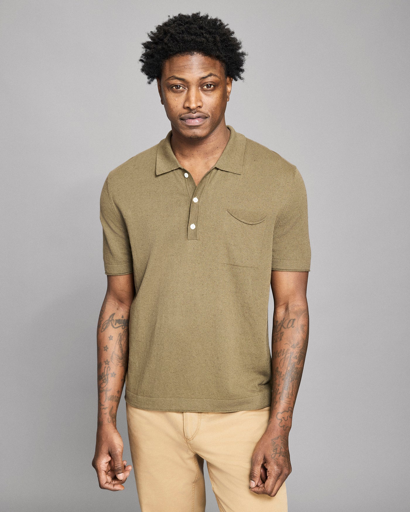 Man wearing a green polo shirt and beige pants against a gray background