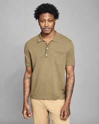 Man wearing a green polo shirt and beige pants against a gray background