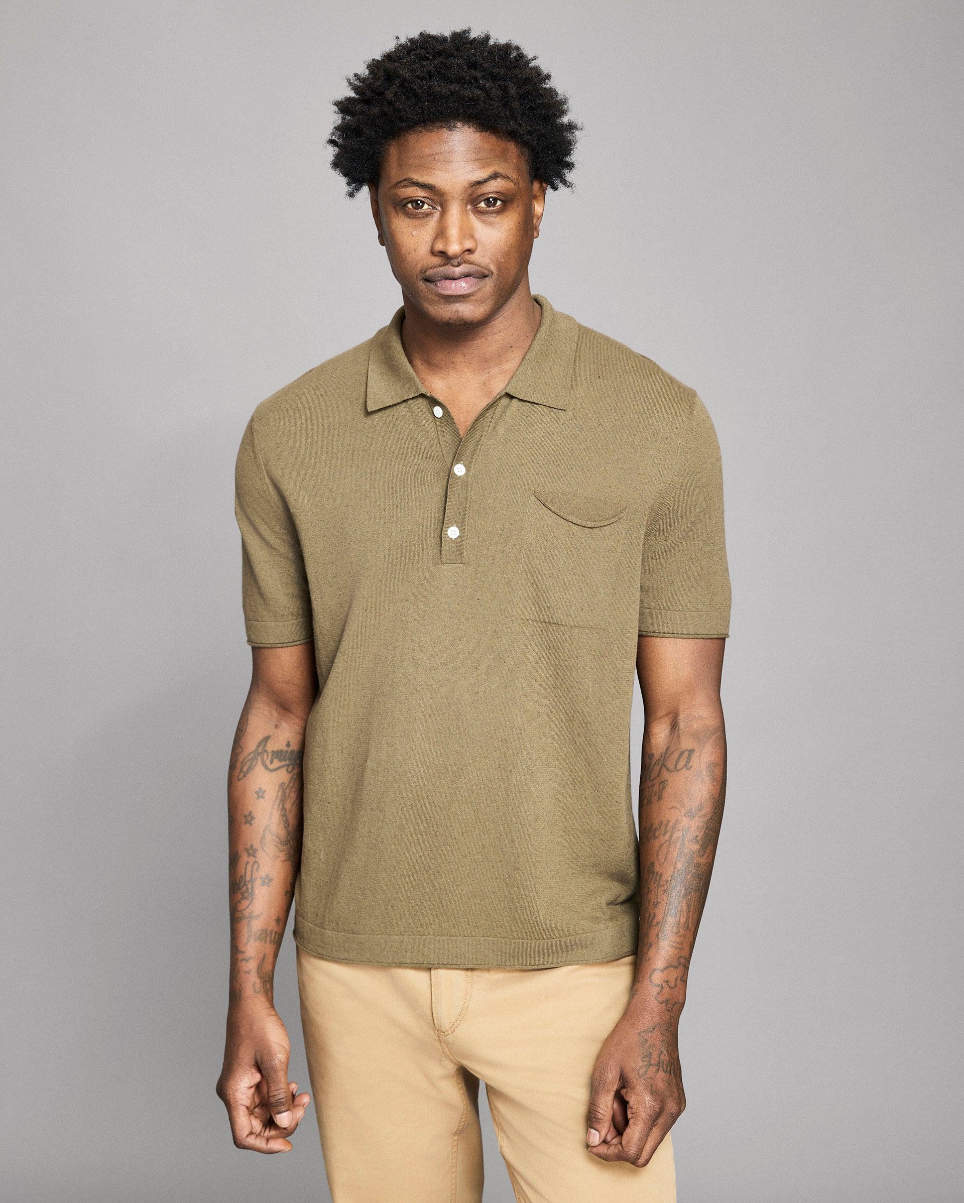 Man wearing a green polo shirt and beige pants against a gray background