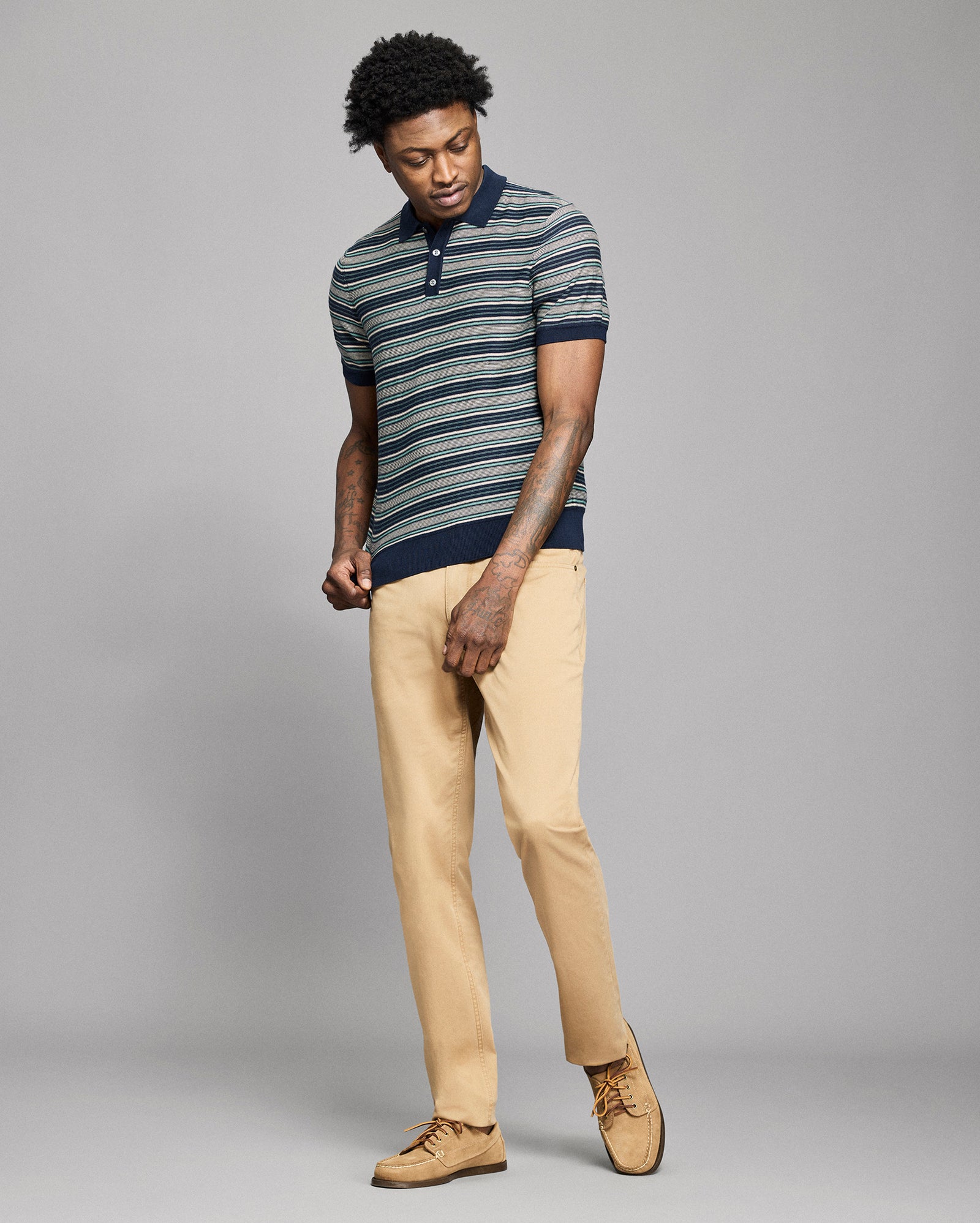 Man wearing a striped polo shirt and beige pants against a gray background