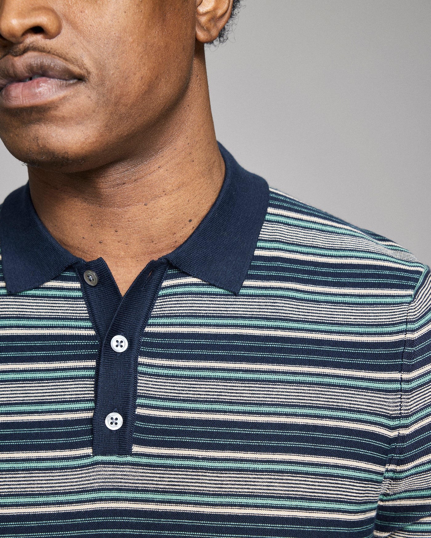 Man wearing a striped polo shirt with a neutral background