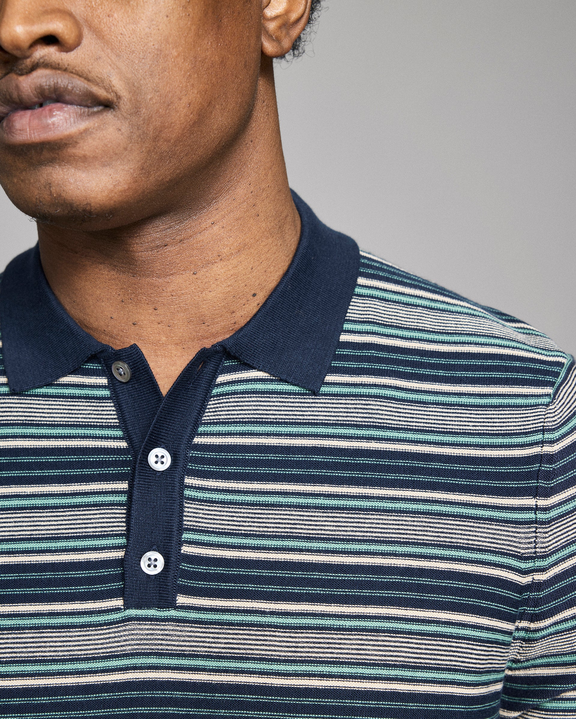 Man wearing a striped polo shirt with a neutral background
