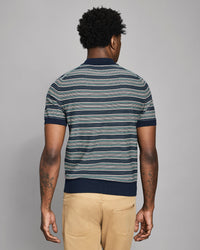 Man wearing a striped polo shirt and beige pants against a gray background