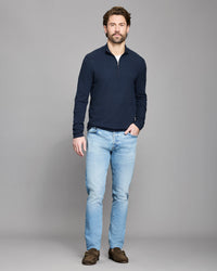 Man wearing a navy sweater and light blue jeans on a gray background
