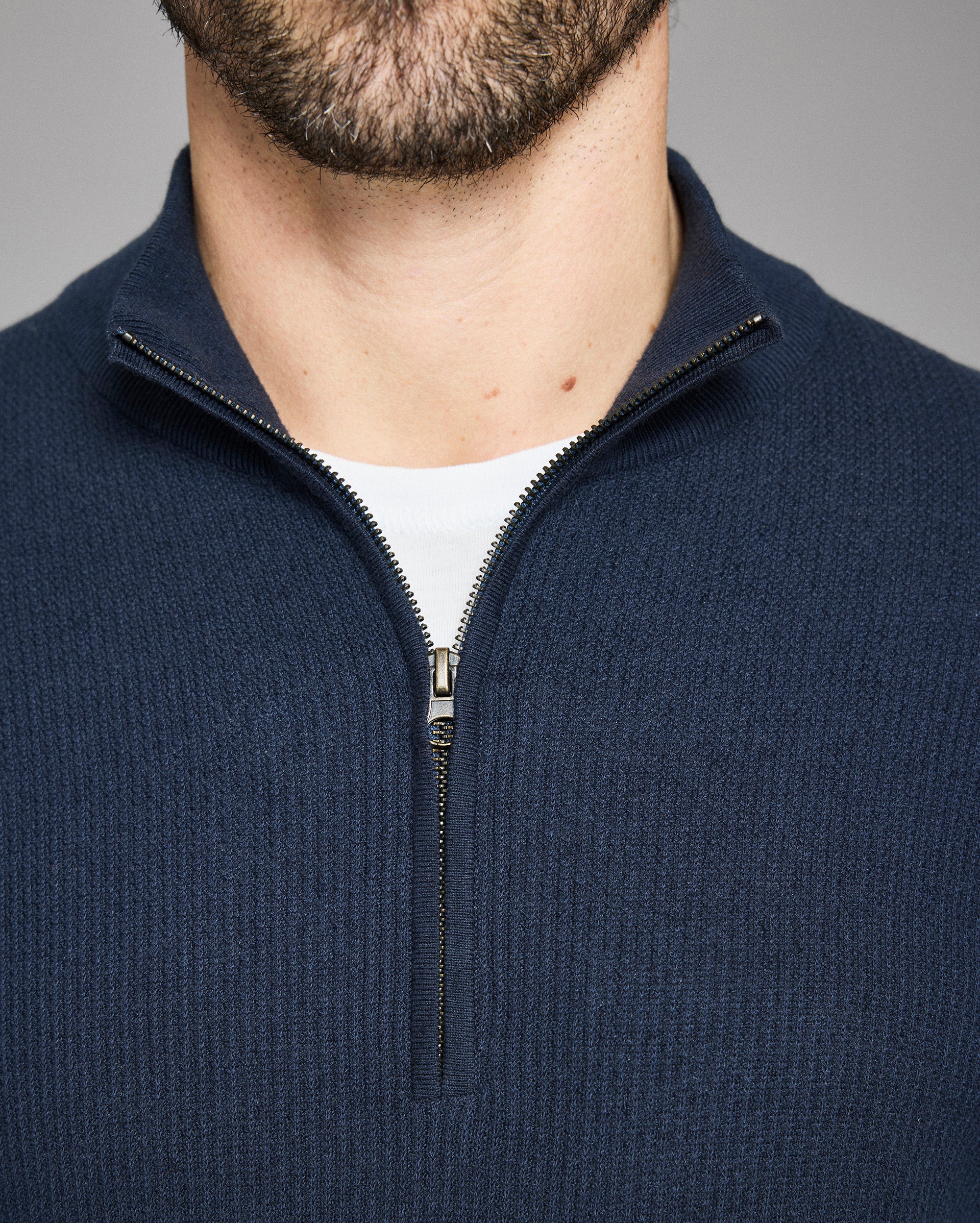 Navy blue zip-up sweater worn by a person on a gray background